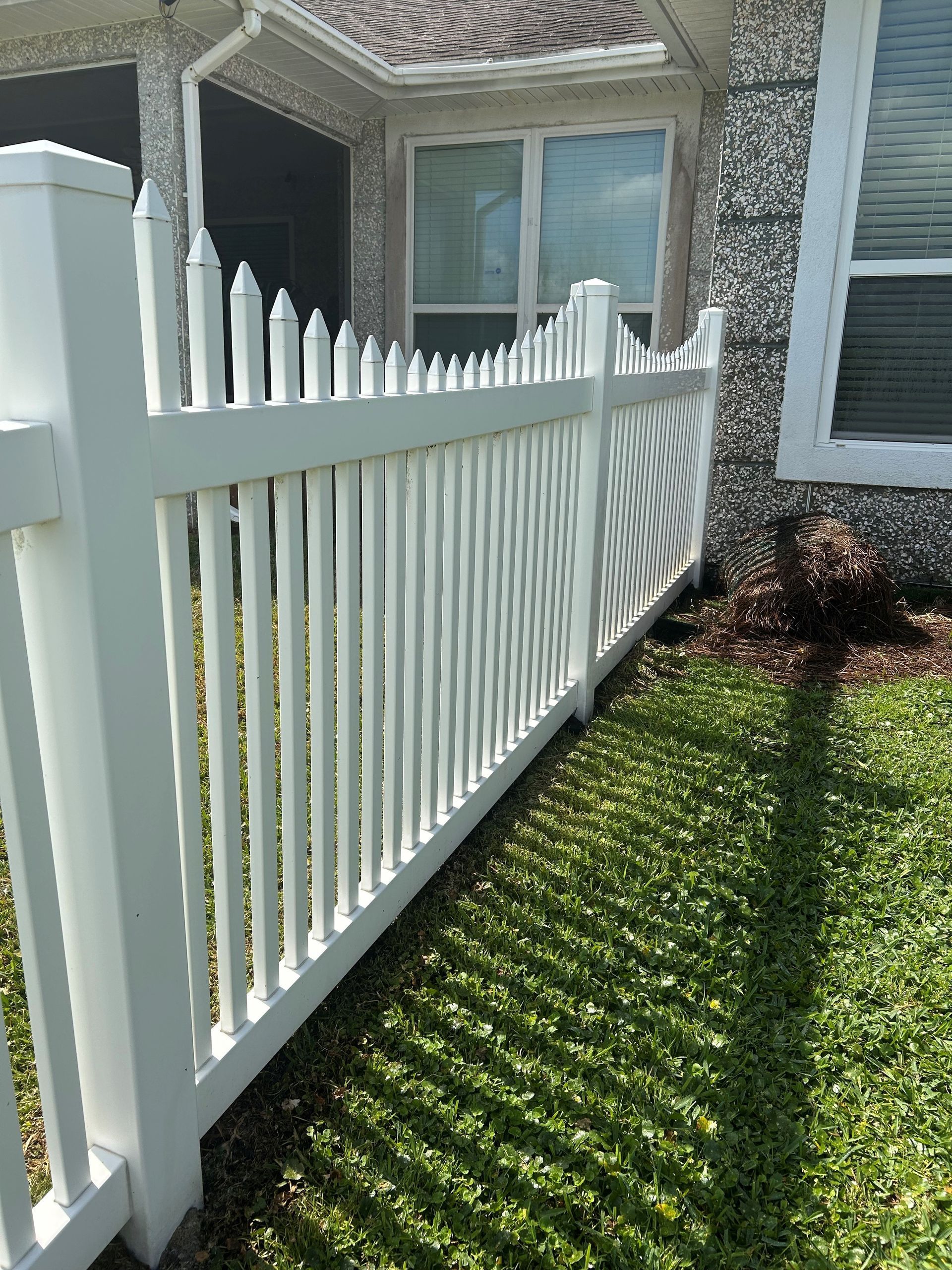 White picket fence next to a house with green grass, sunny day.