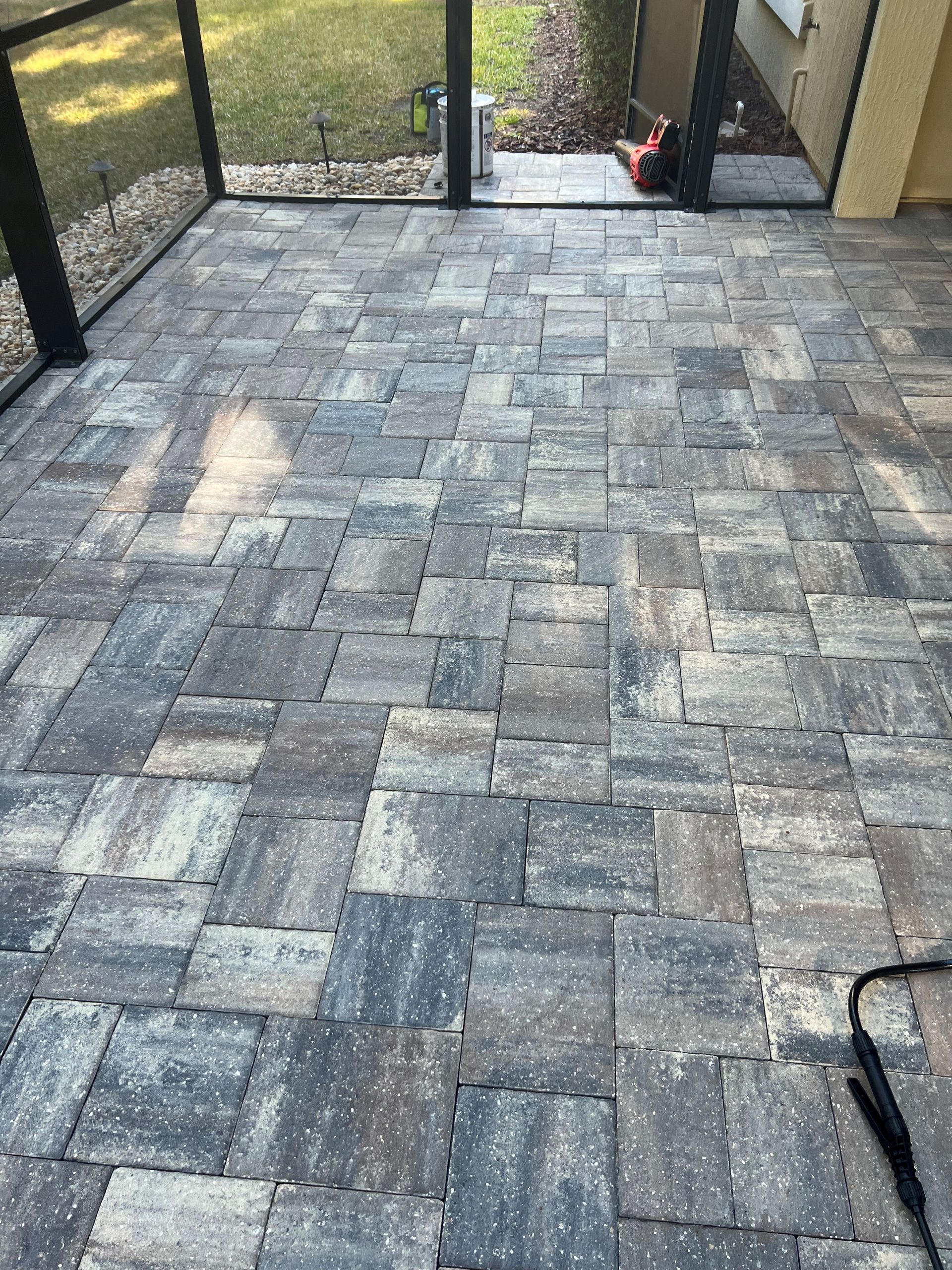 Brick paver patio with gray, black, and tan tones under a screened porch.