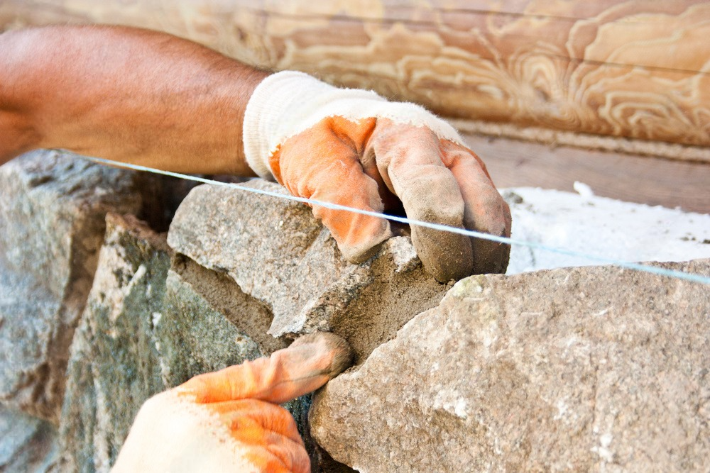 a man wearing orange gloves is working on a stone wall .