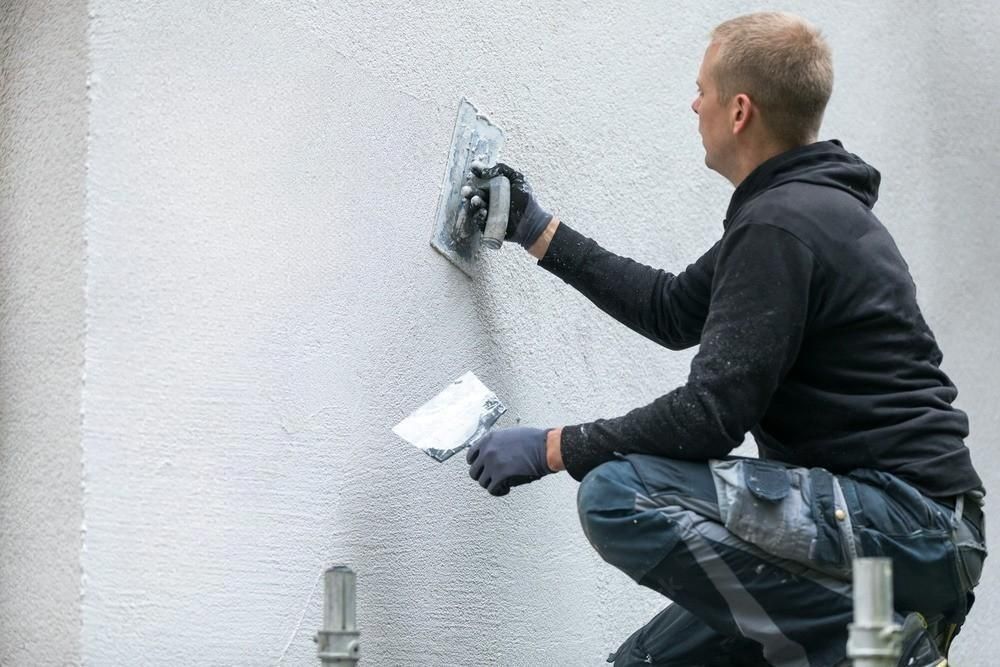 a man is kneeling down and plastering a wall with a spatula .