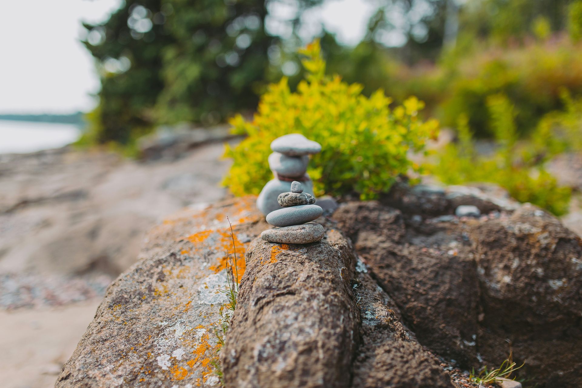 Stack of gray stones balanced on a large rock, with green and yellow foliage in the background.