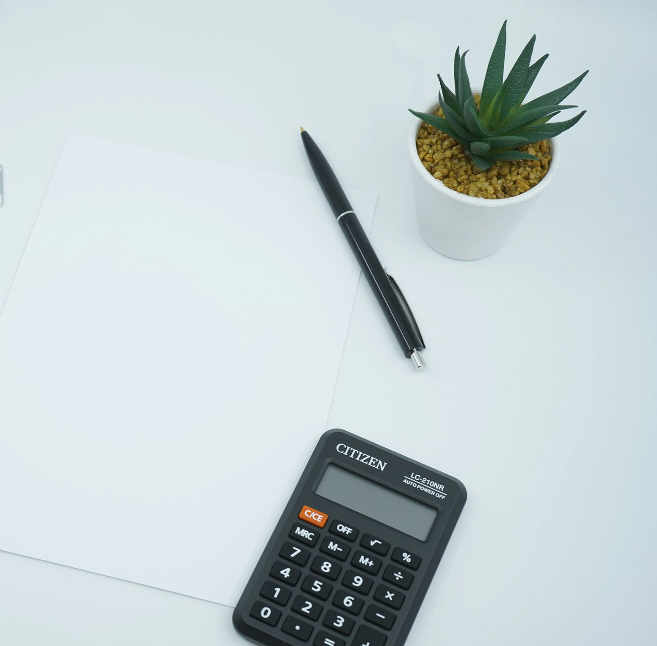 Person using a scientific calculator on a white surface with laptop, papers, and pens.
