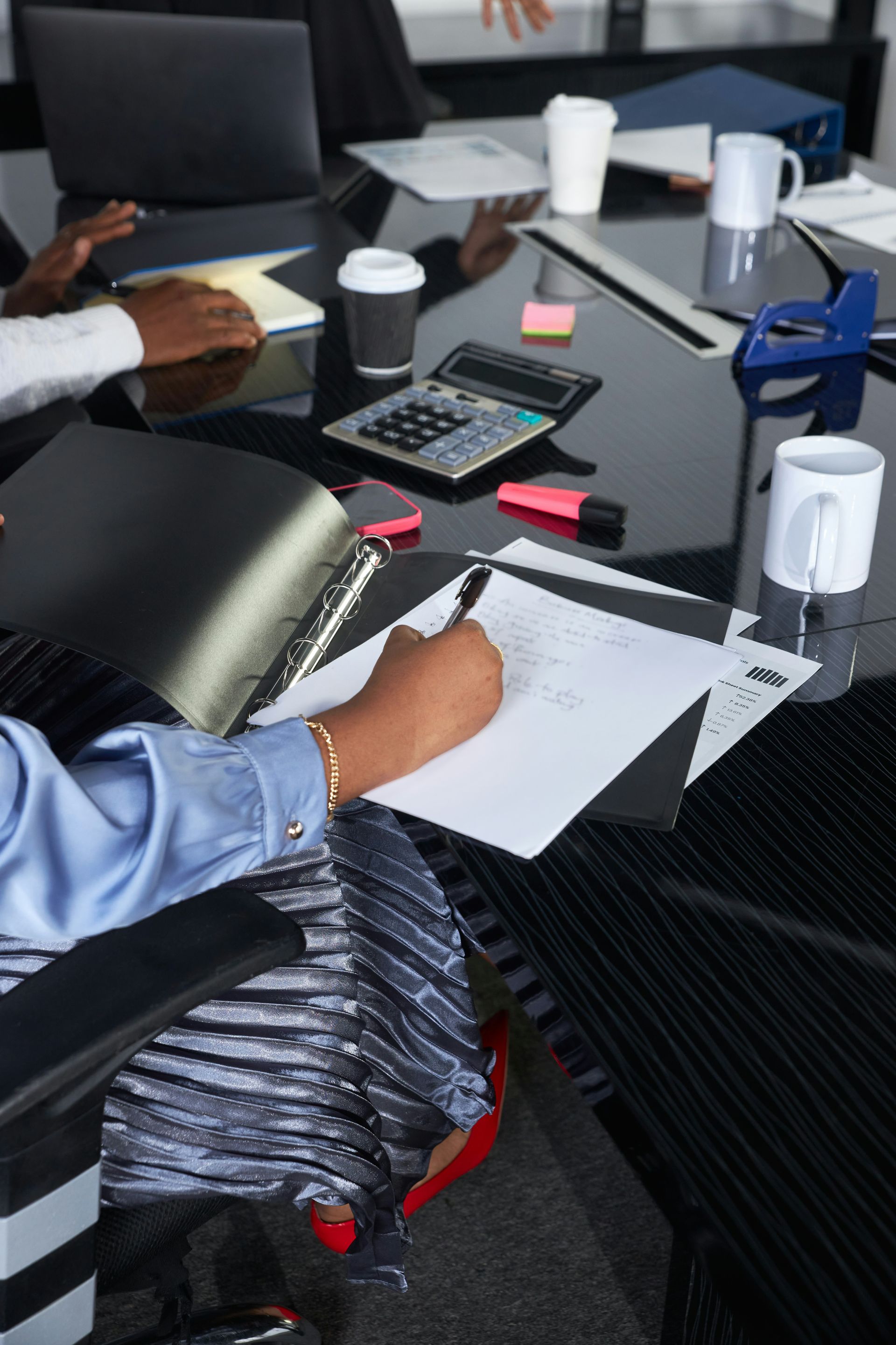Two women at a desk reviewing documents with laptops, calculator, and pen, focused discussion.