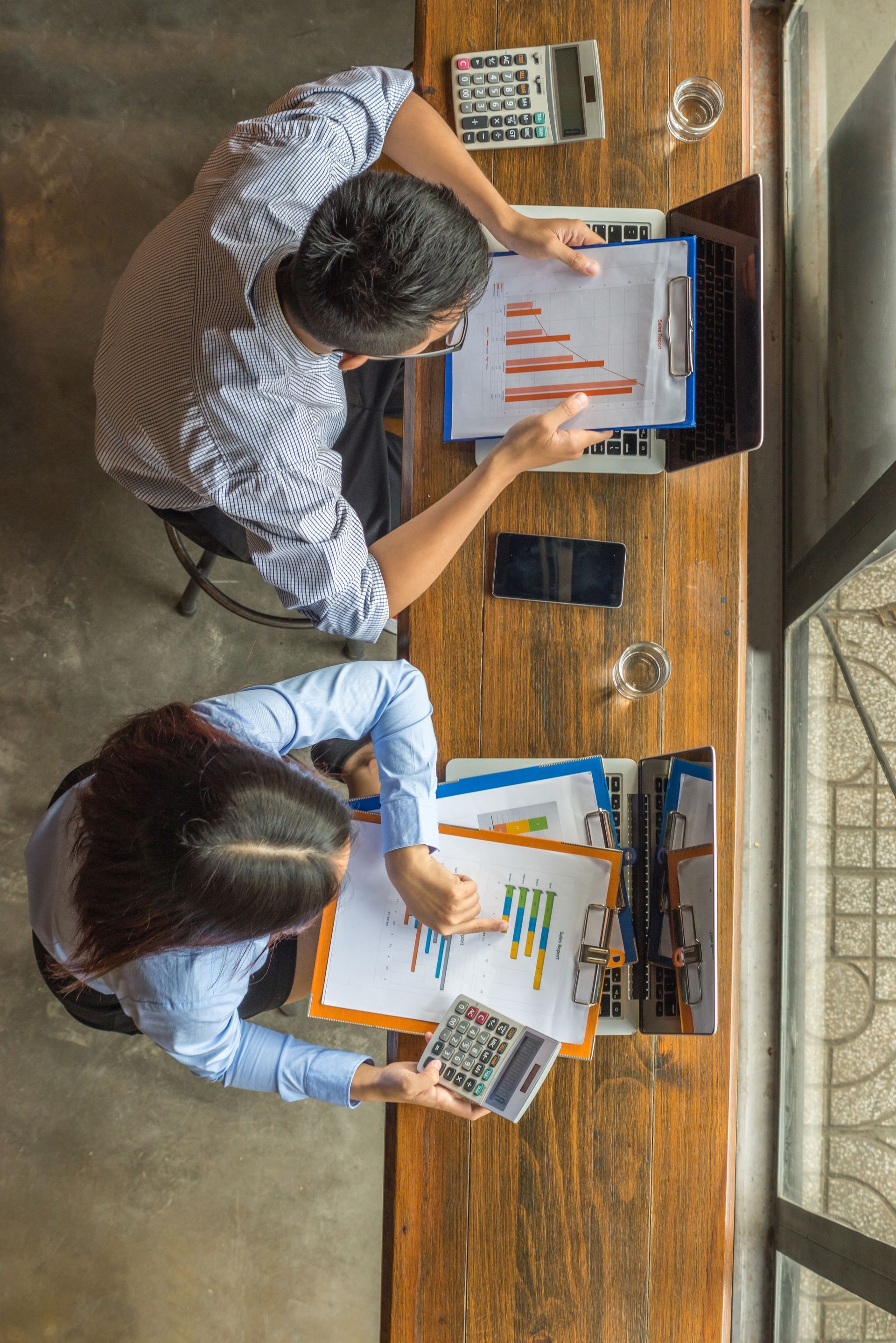 Woman arranging flowers at a wooden table, blue wall background, bright flowers.