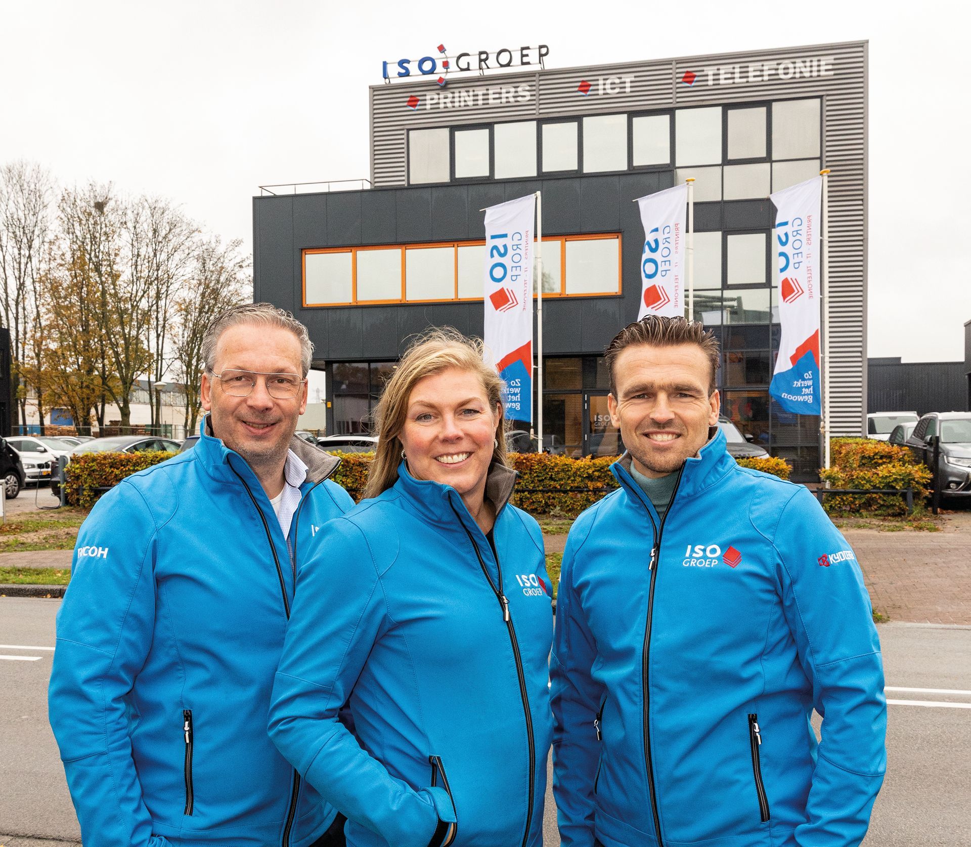 three people wearing iso group jackets stand in front of a building