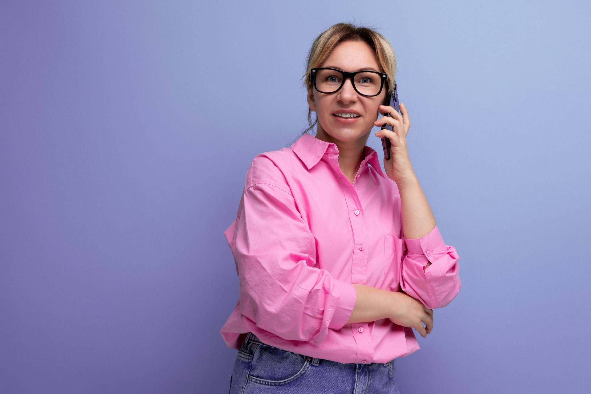 a woman wearing glasses and a pink shirt is talking on a cell phone