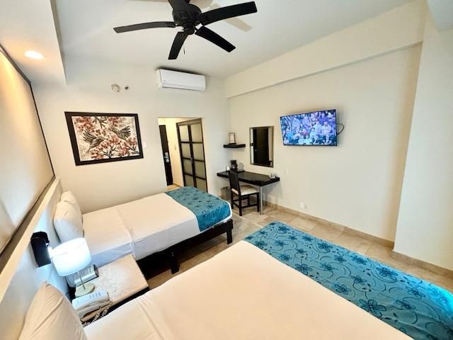 Una habitación de hotel con dos camas, un escritorio, un televisor y un ventilador de techo.