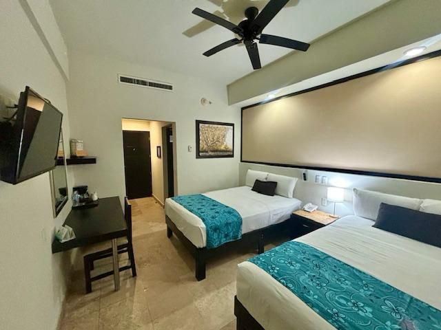 Una habitación de hotel con dos camas, un escritorio, un televisor y un ventilador de techo.