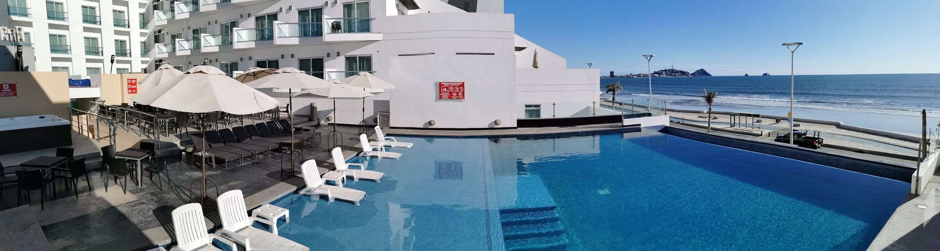 Una gran piscina está rodeada de sillas y sombrillas frente a un hotel.