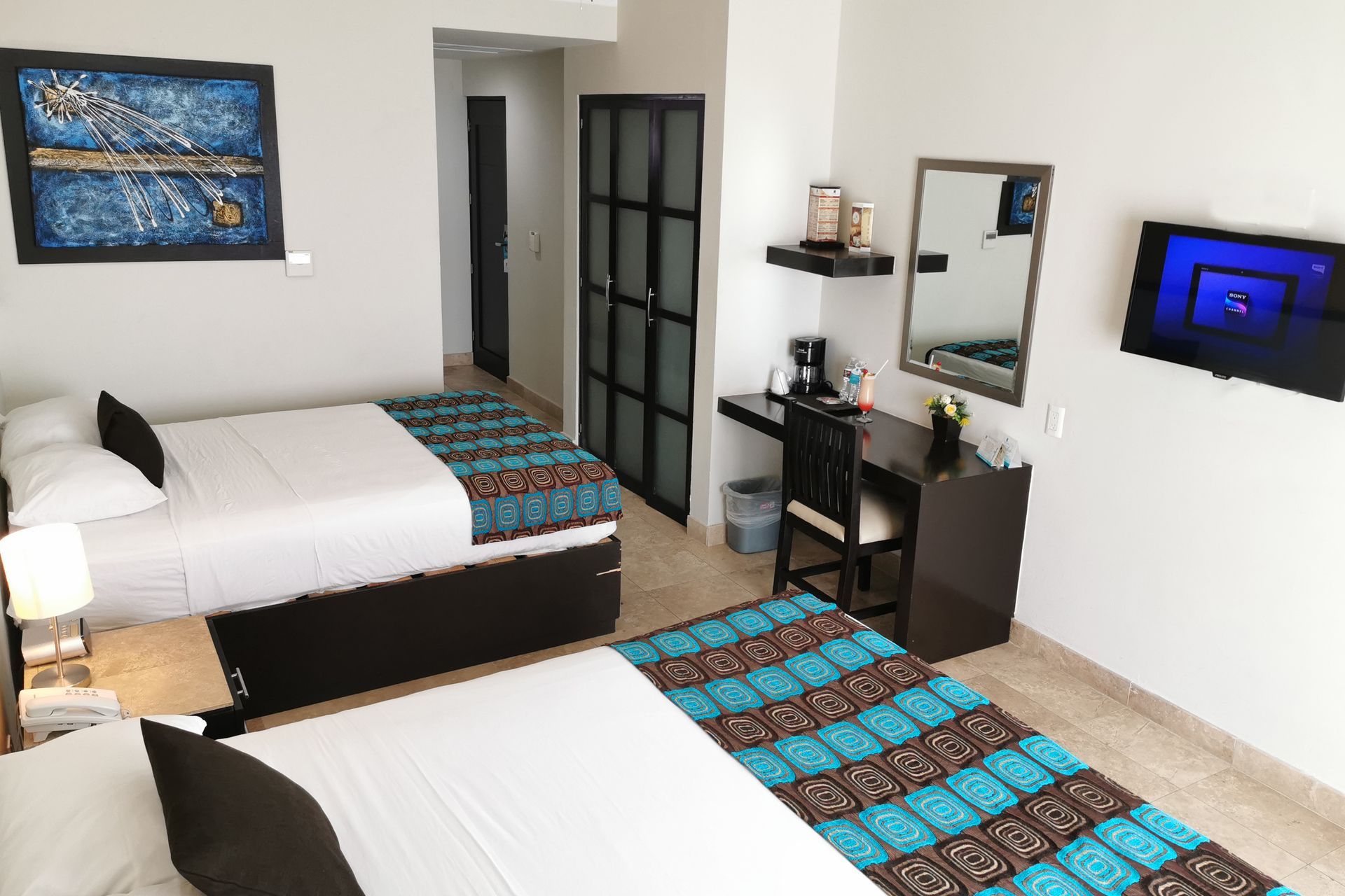 Una habitación de hotel con dos camas, un escritorio, un televisor y un espejo.
