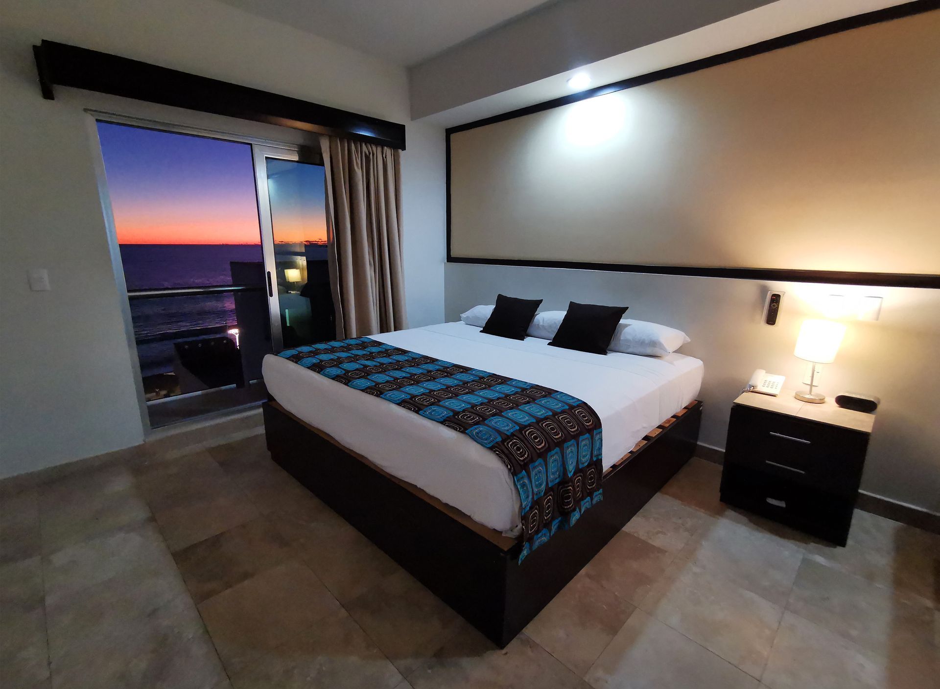Una habitación de hotel con una cama grande y un balcón con vista al océano.