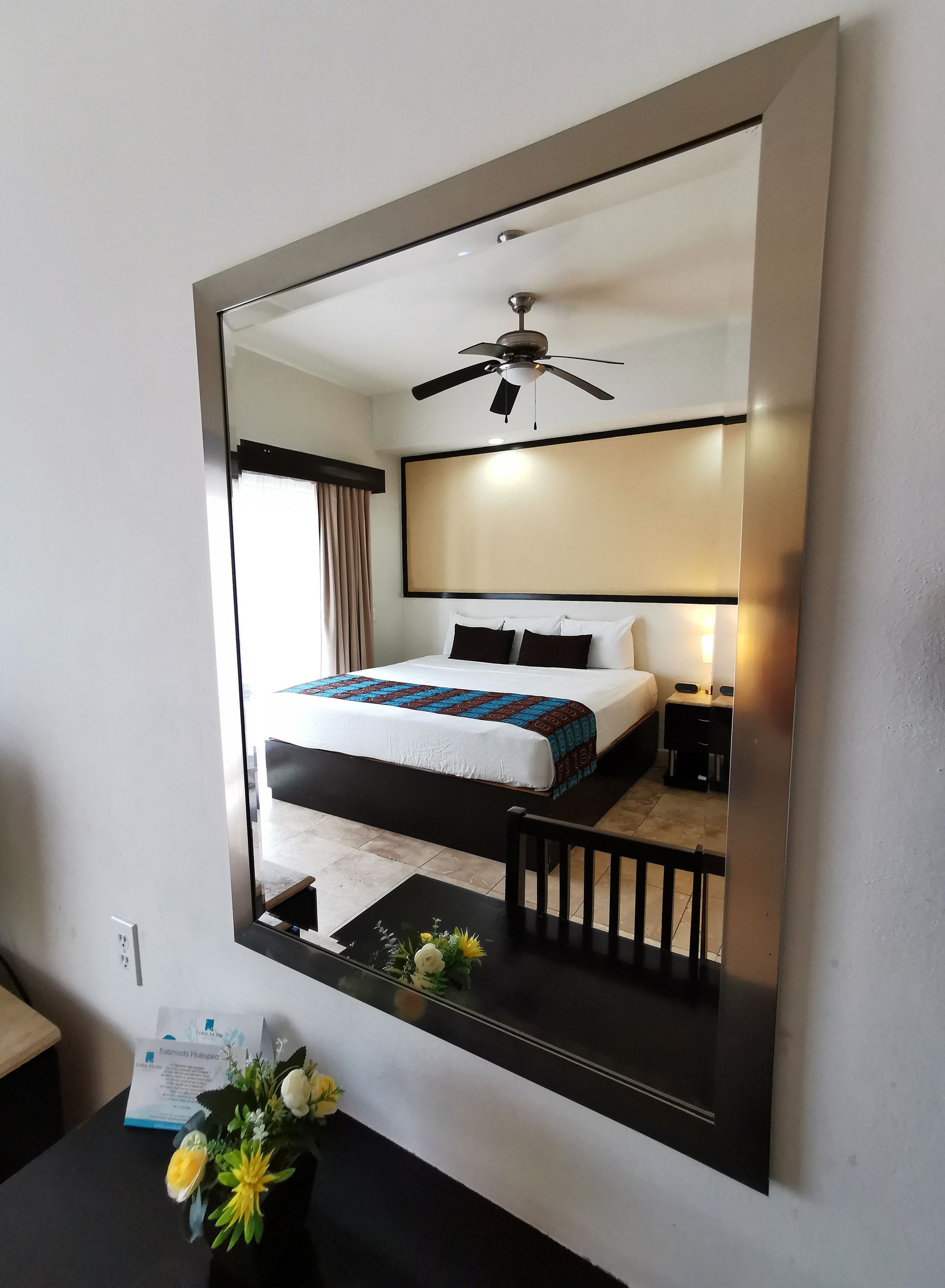 Un dormitorio con una cama king size y un ventilador de techo se refleja en un espejo.