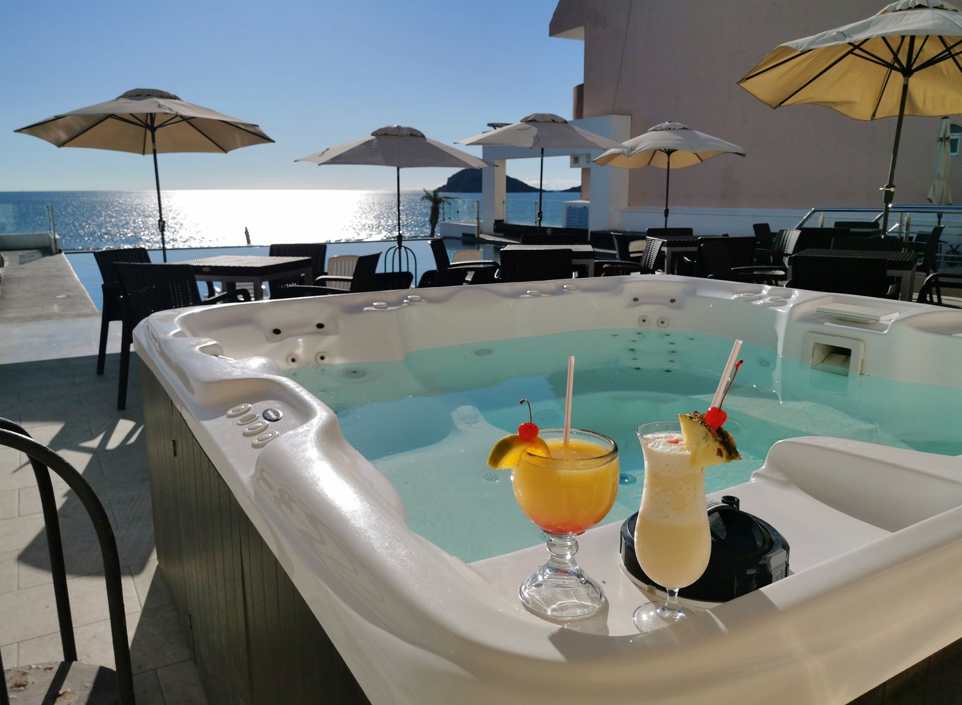 Un jacuzzi con dos bebidas y sombrillas al fondo.