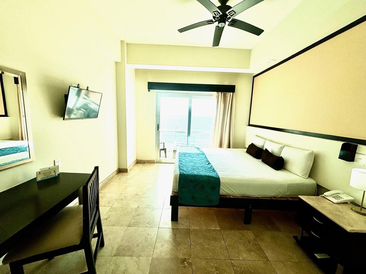 Una habitación de hotel con una cama tamaño king, escritorio, silla y televisión.