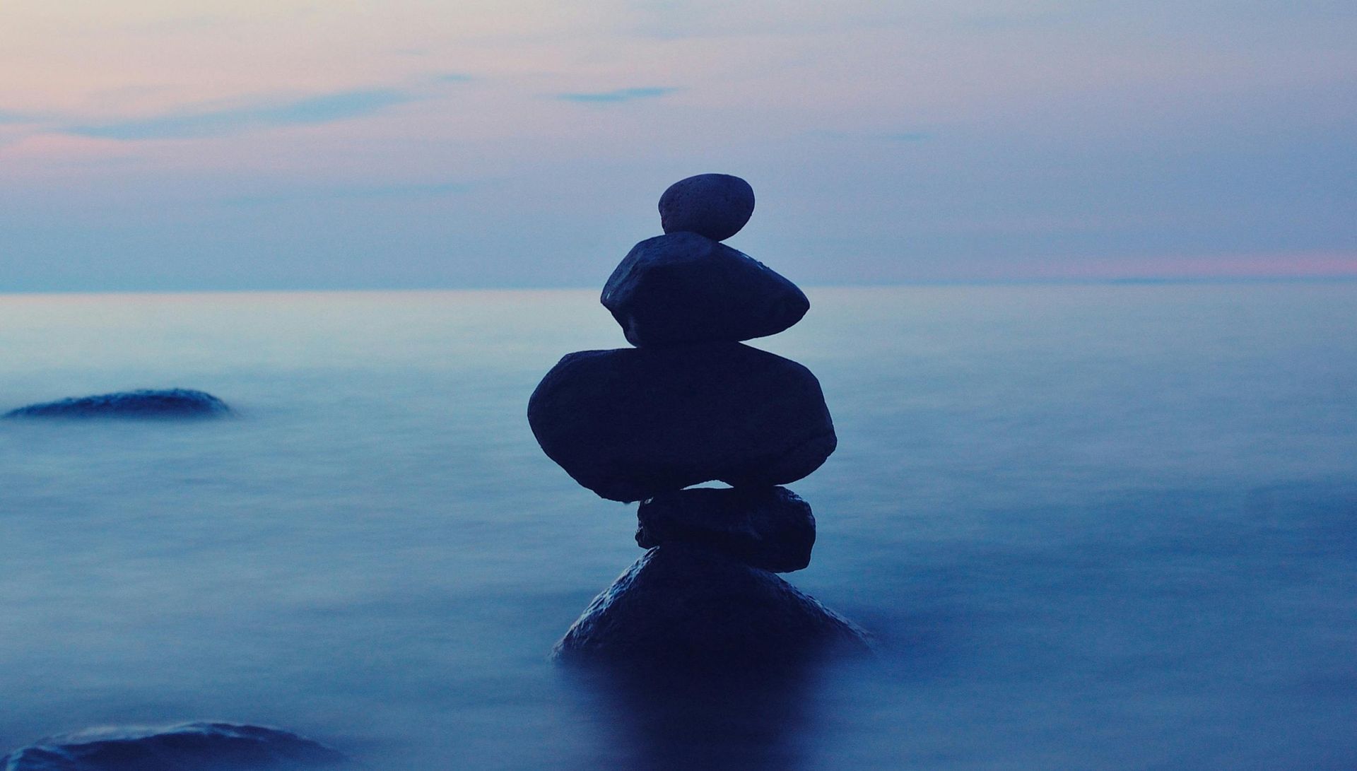 Stack of balanced stones in calm, blue water, reflecting the soft twilight sky.