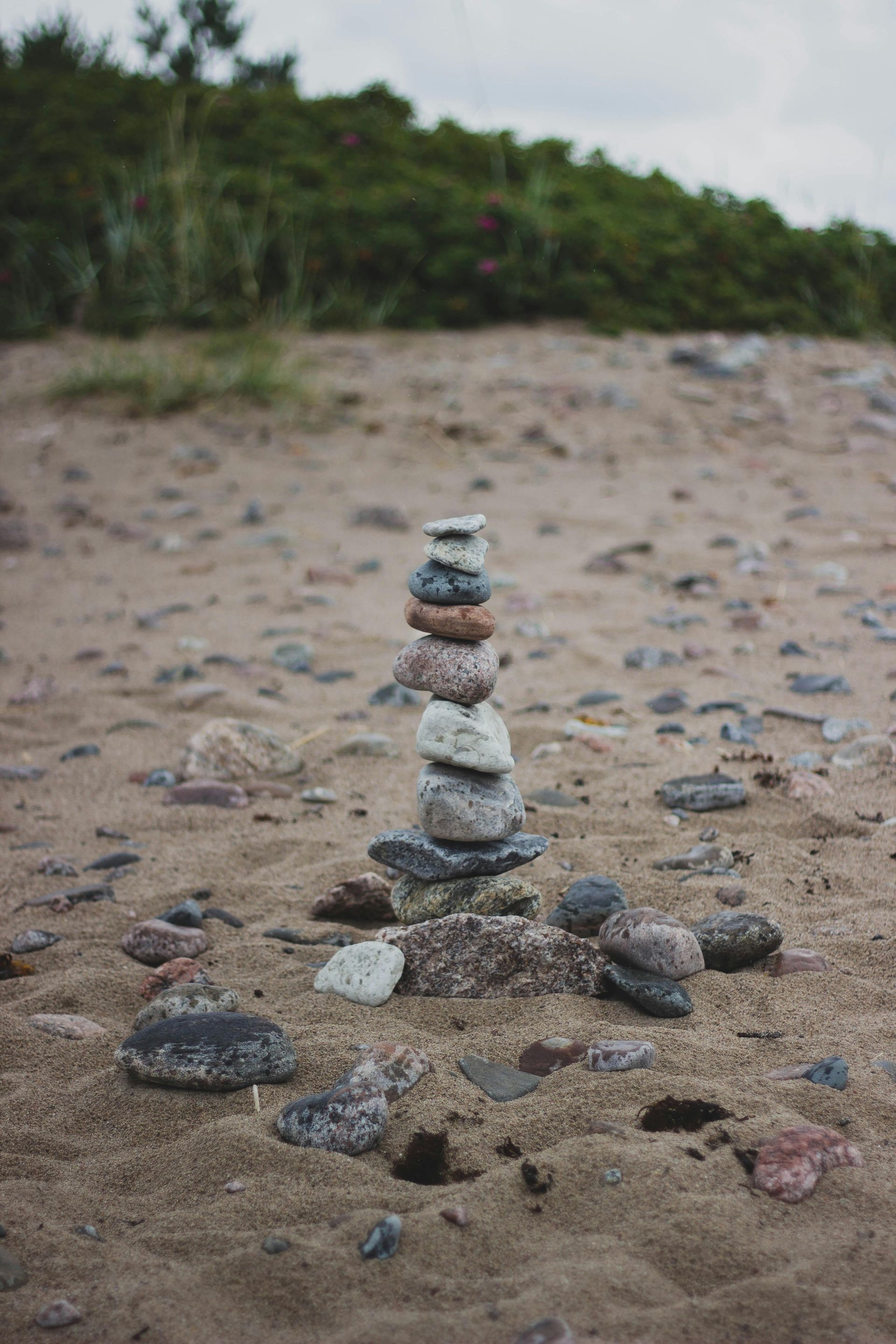 Stone cairn on a sandy beach, with green foliage in the background.