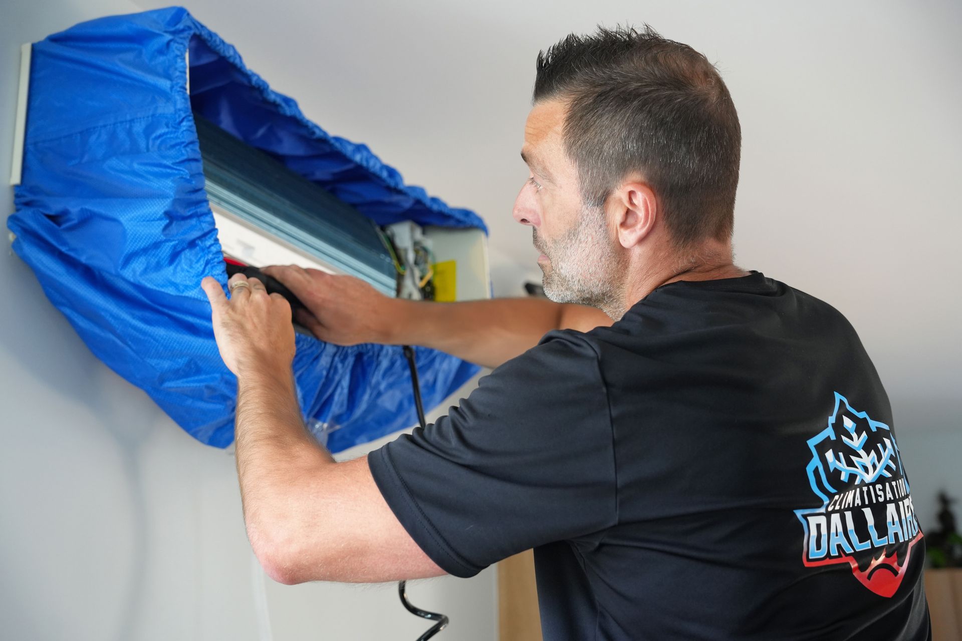 Un homme nettoie un climatiseur avec un couvercle bleu.
