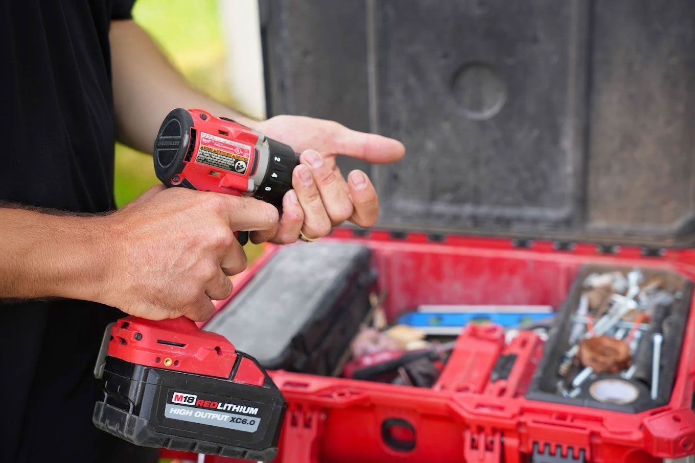 Un homme tient une perceuse dans ses mains devant une boîte à outils.