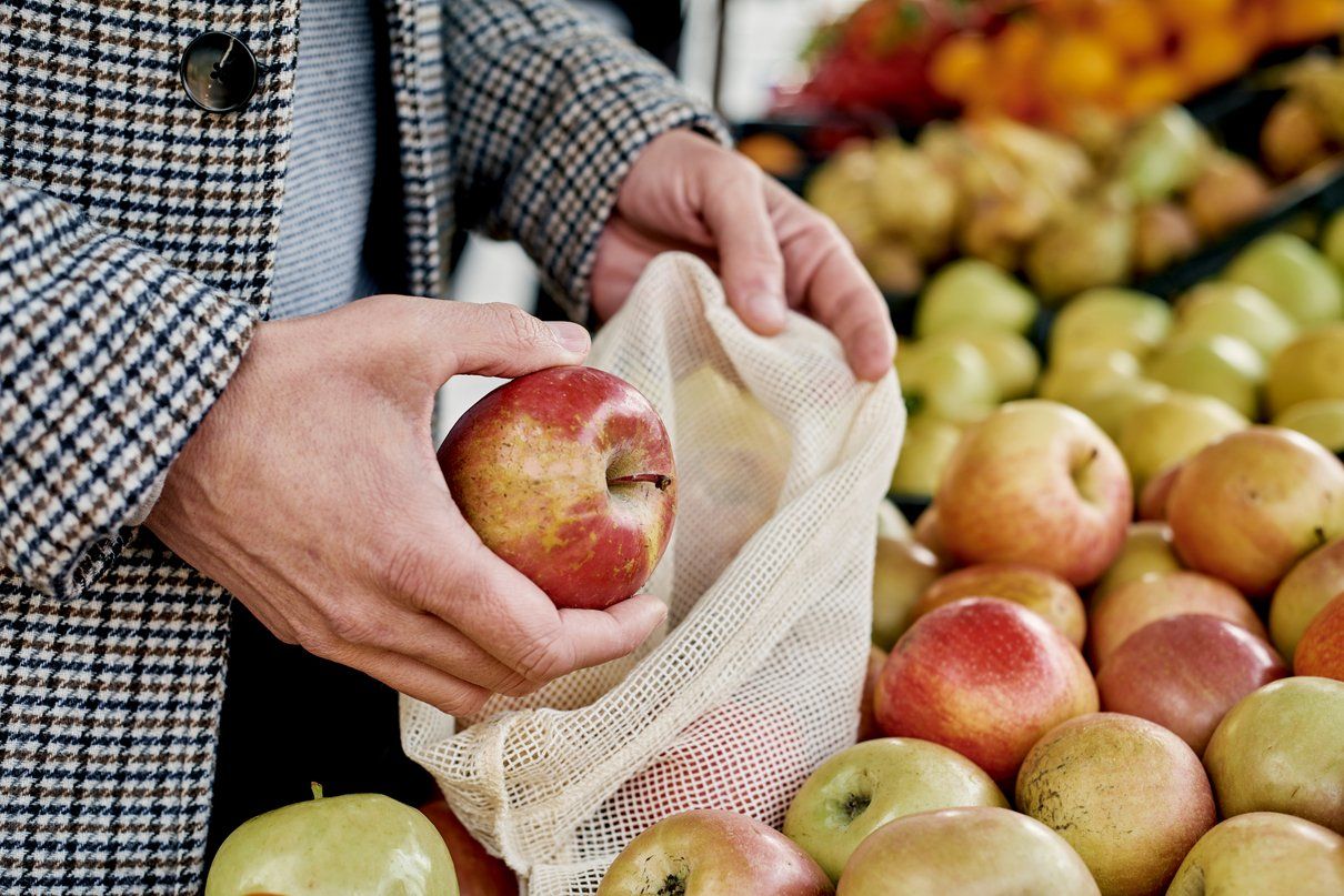A shopper using a reusable muslin bag to purchase apples.