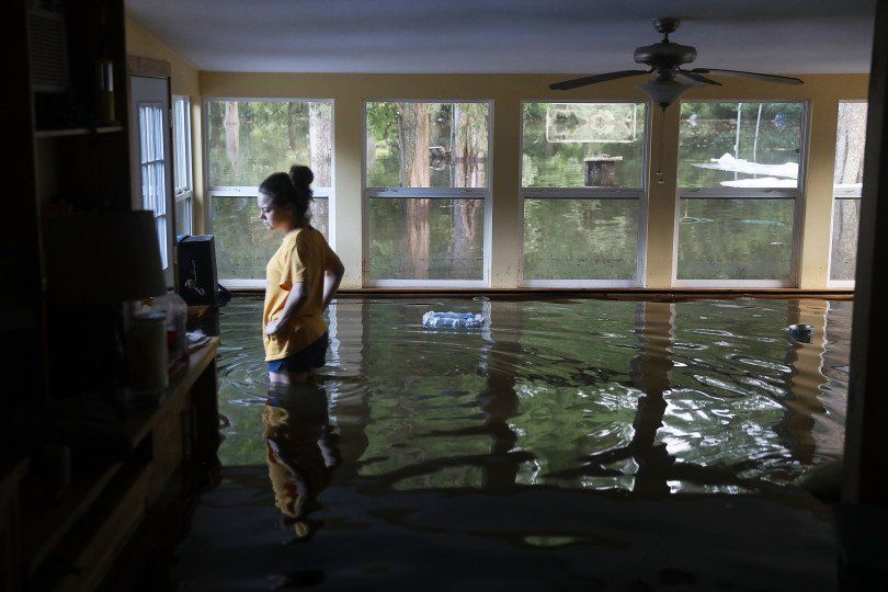 A woman is standing in a flooded room with a ceiling fan.