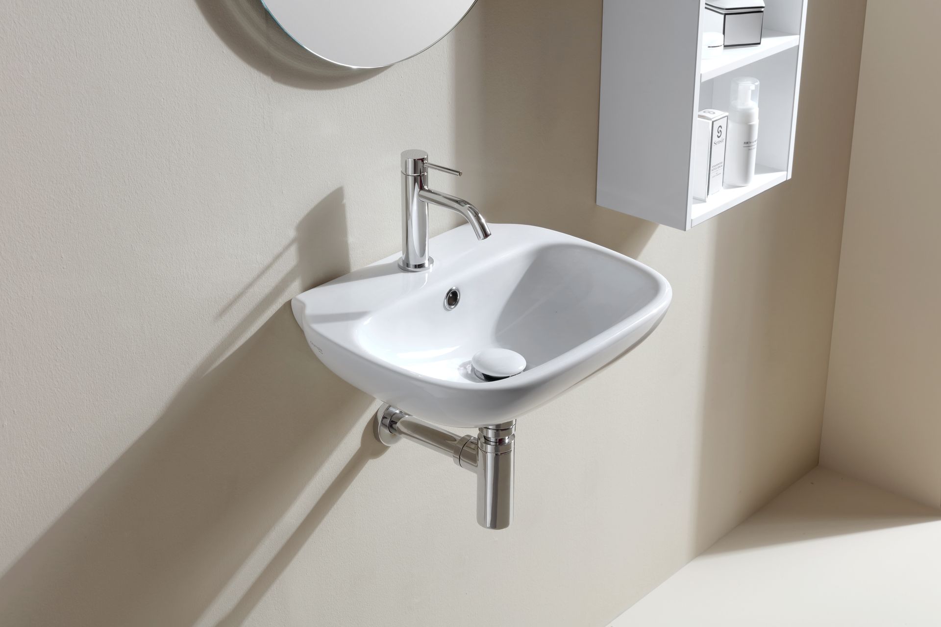 Lavandino bianco a parete con rubinetto cromato e scarico. Bagno con mobiletto bianco e specchio.