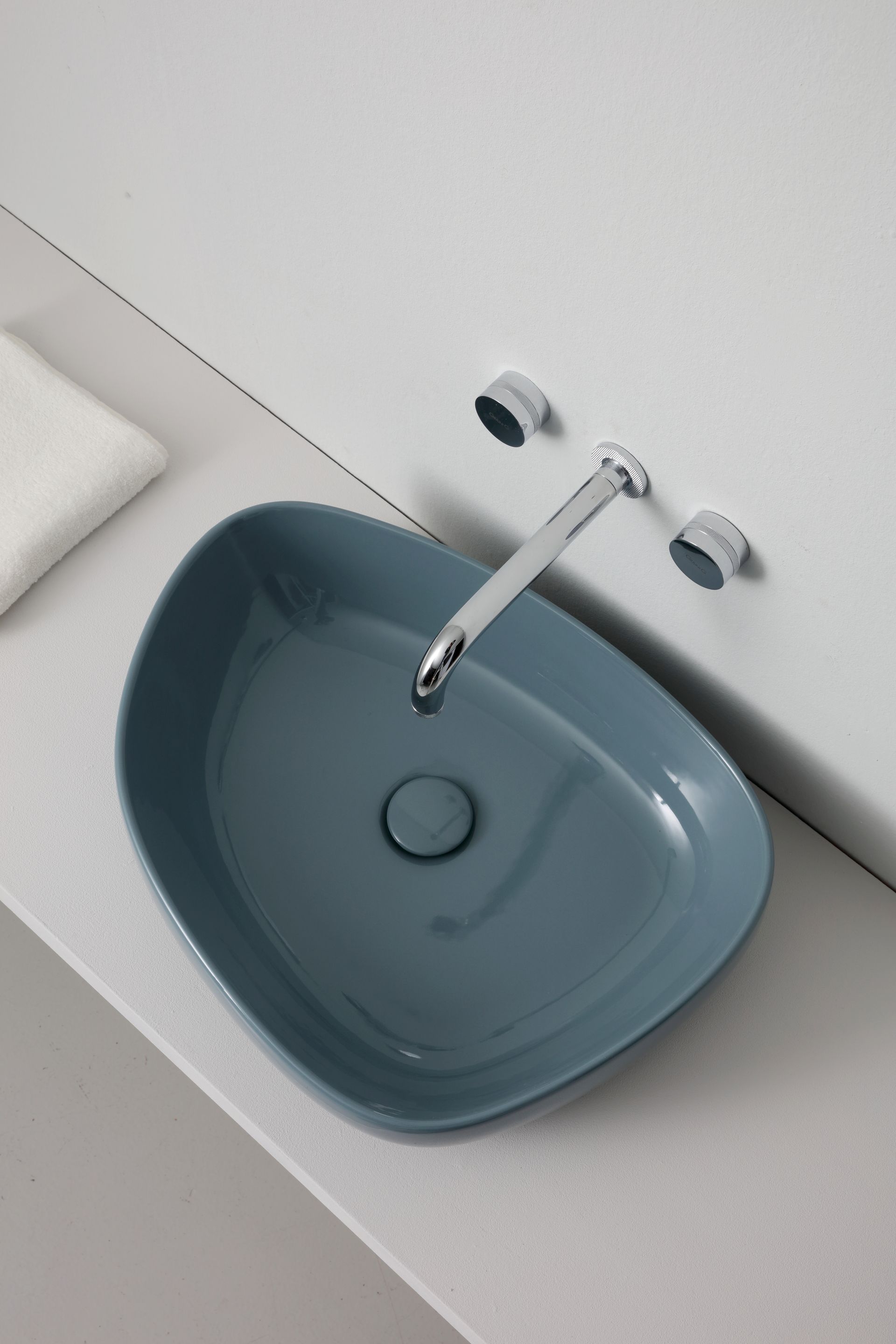 Lavandino in ceramica blu dalla forma organica con rubinetto cromato. Piano di lavoro e parete bianchi.