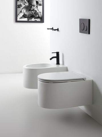 Moderno bagno bianco con WC e bidet sospesi, sanitari neri e un'opera d'arte.