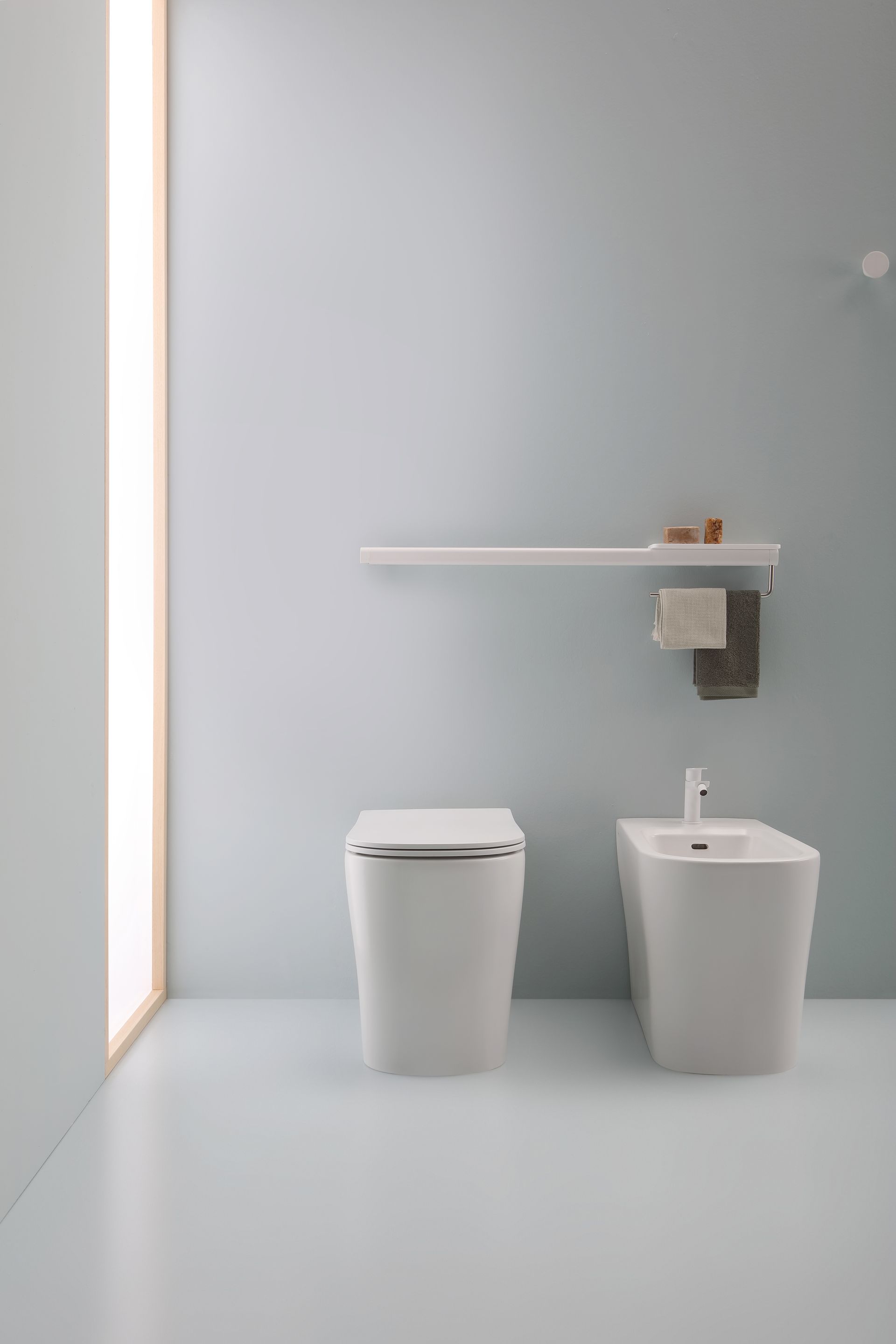 Bagno con WC, bidet e mensola contro una parete azzurra. Design pulito.
