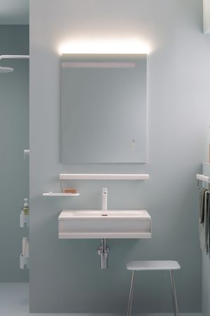 Bagno moderno con lavandino bianco, specchio con luce sopraelevata e un piccolo sgabello. Pareti azzurre.