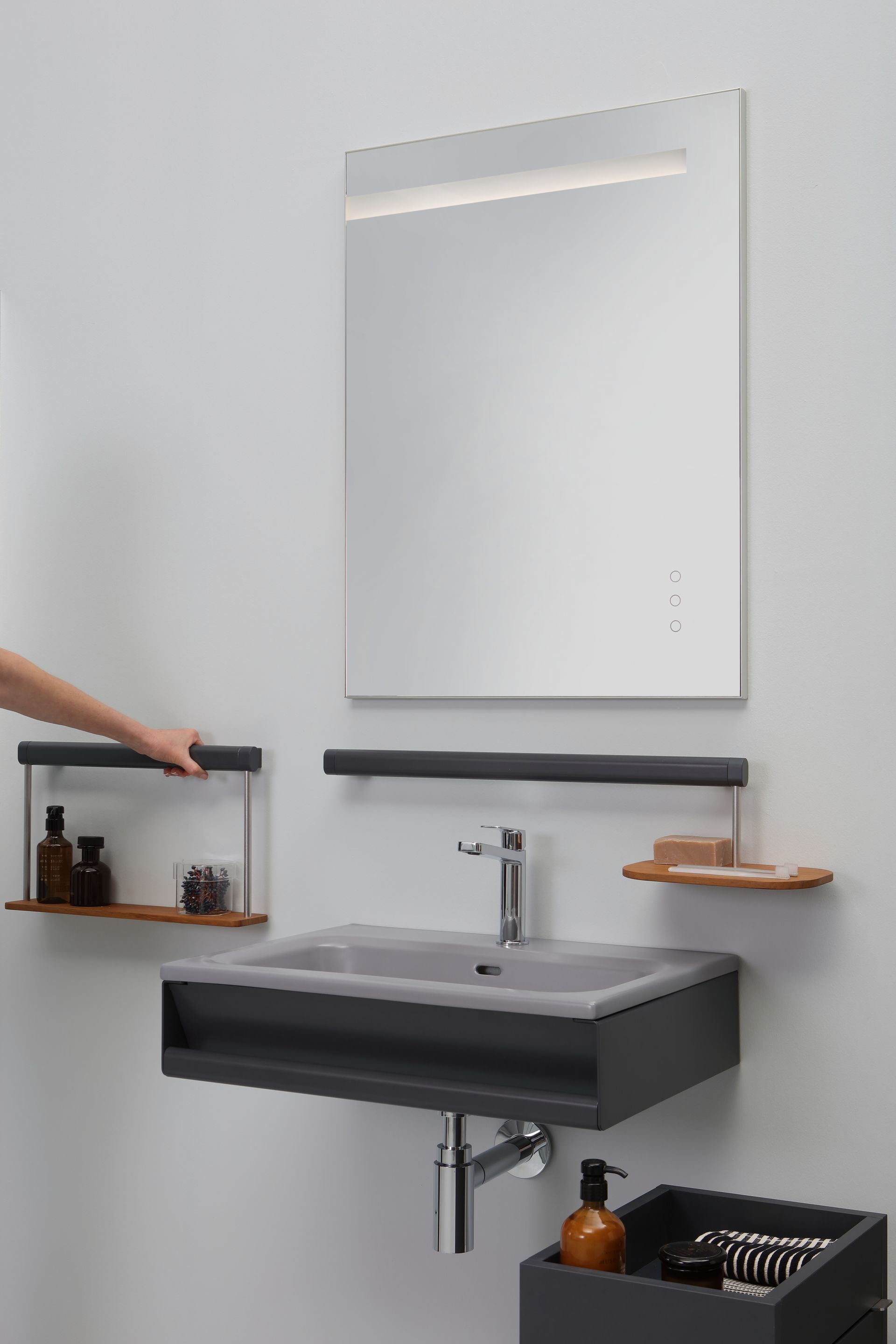 Mobile da bagno moderno con lavandino grigio, specchio, mensole e una mano che allunga la mano verso una mensola.