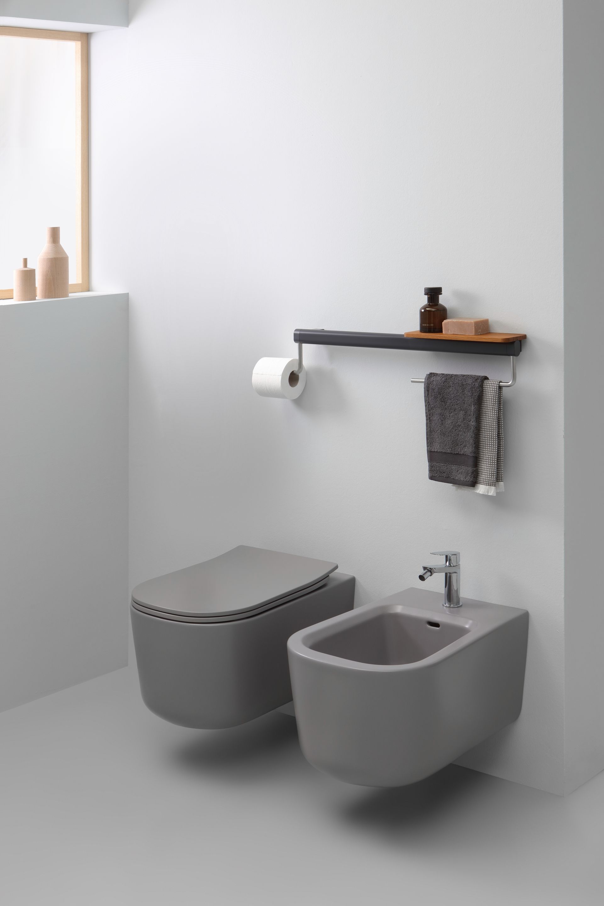 WC e bidet grigi in un bagno moderno, con una mensola per articoli da toeletta e asciugamani.