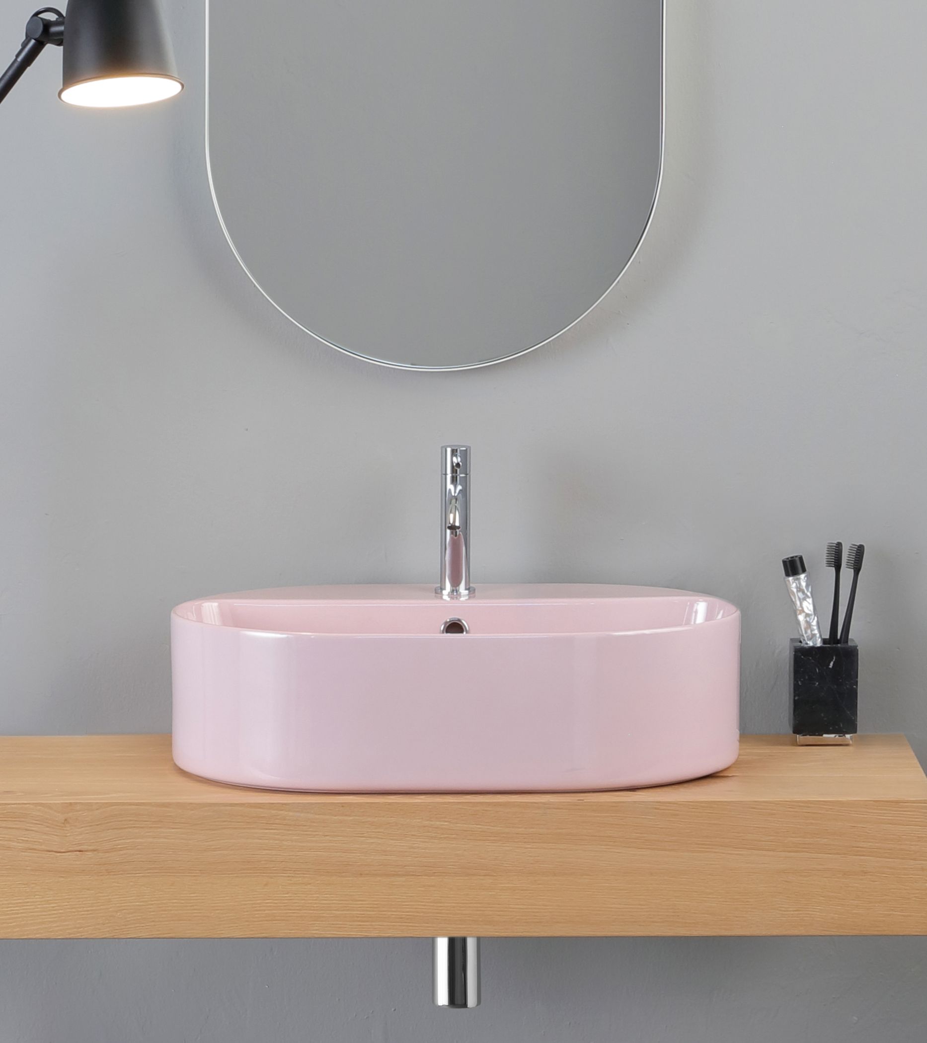 Lavandino rettangolare rosa su una mensola di legno, con rubinetto cromato e specchio circolare.