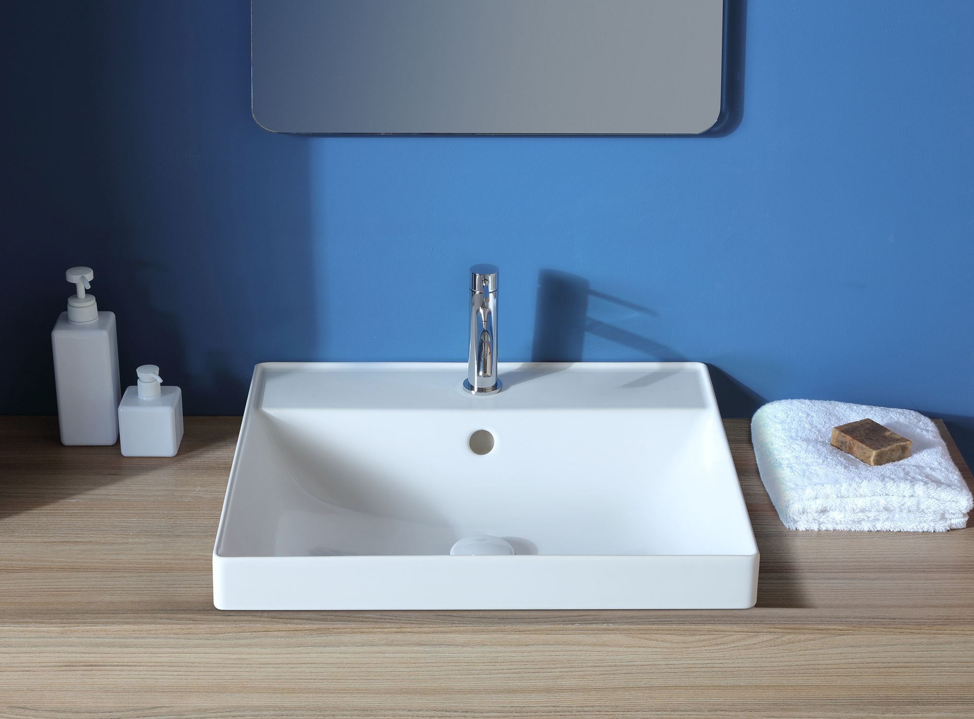 Lavandino rettangolare bianco con rubinetto cromato, su un bancone in legno, con parete blu.