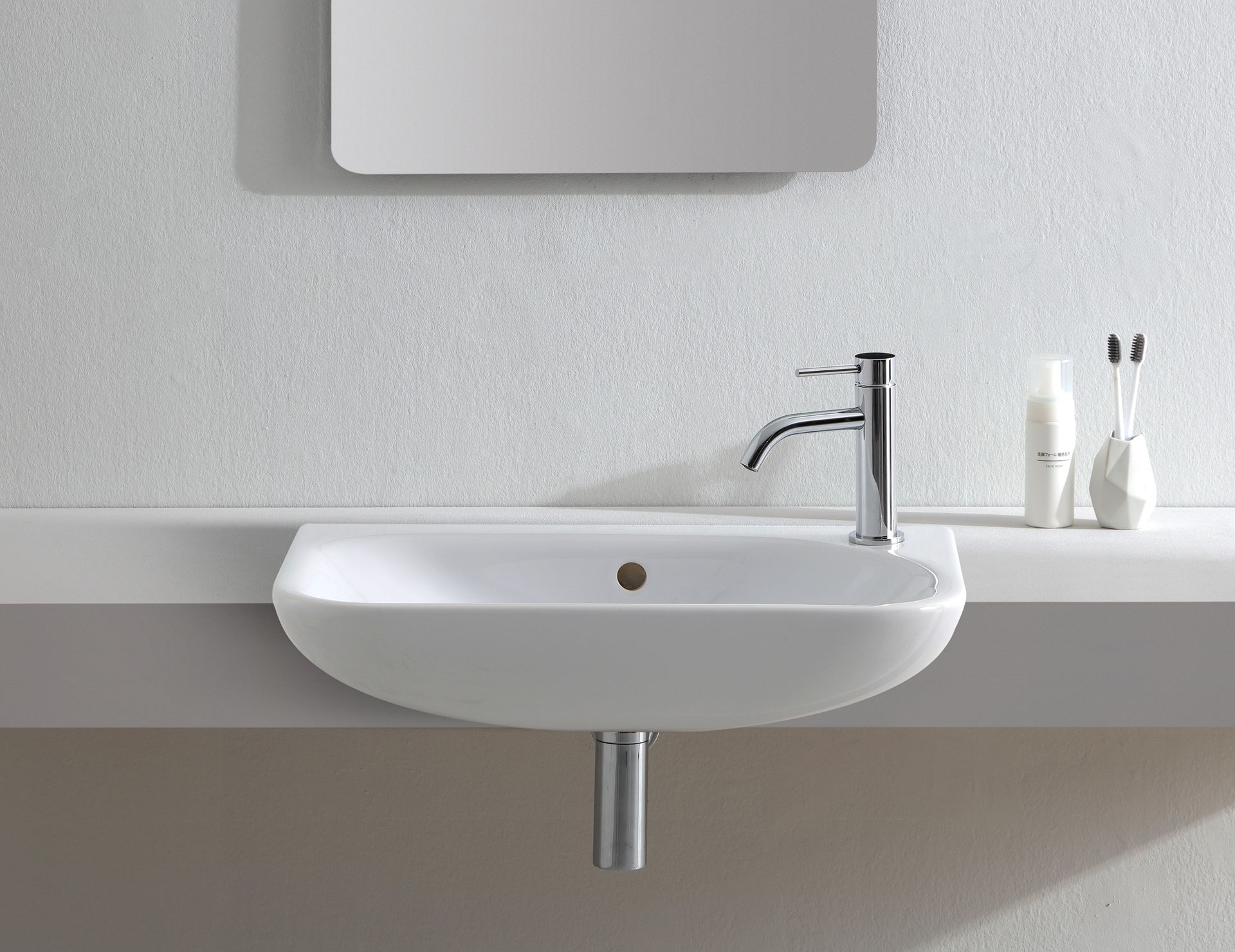 Lavandino bianco del bagno con rubinetto cromato, sotto uno specchio, con articoli da toeletta.
