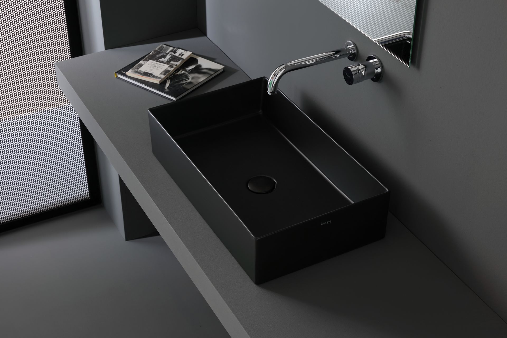 Lavandino rettangolare nero su un ripiano grigio con rubinetto metallico e un libro.