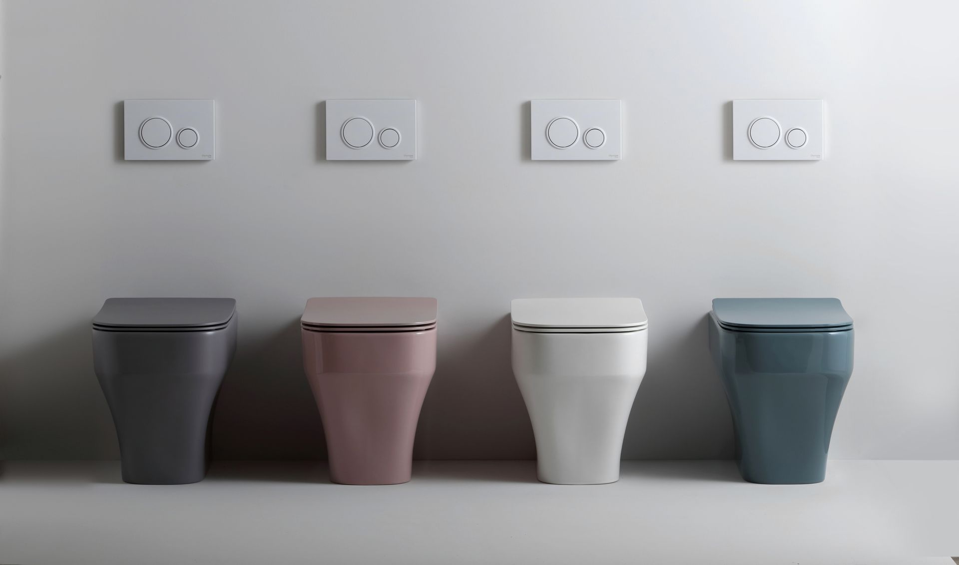 Quattro moderni servizi igienici in colori diversi con placche di scarico abbinate alla parete.