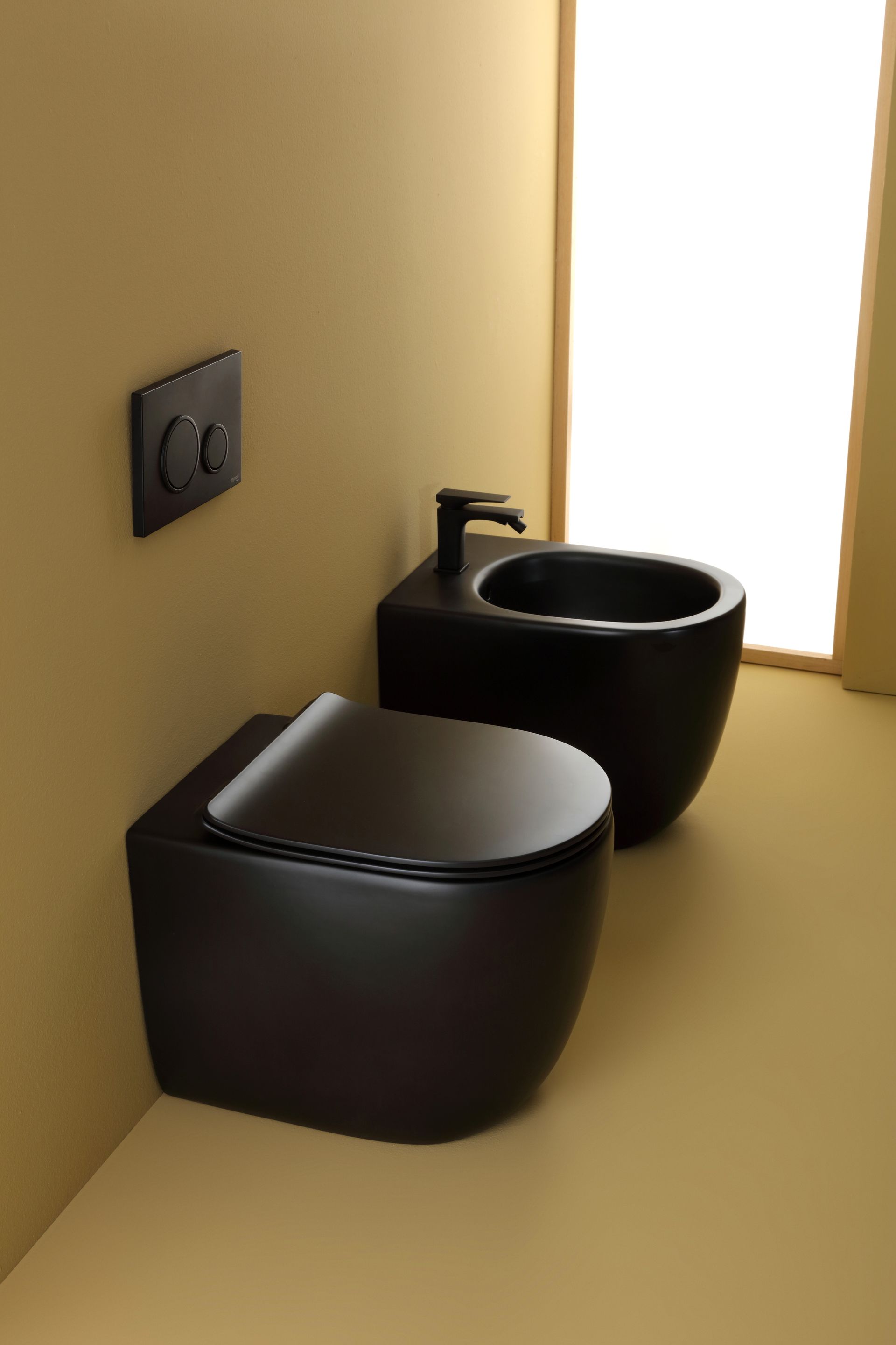 WC e bidet neri in un angolo del bagno, accanto a una finestra. Sanitari neri opachi su pareti gialle.