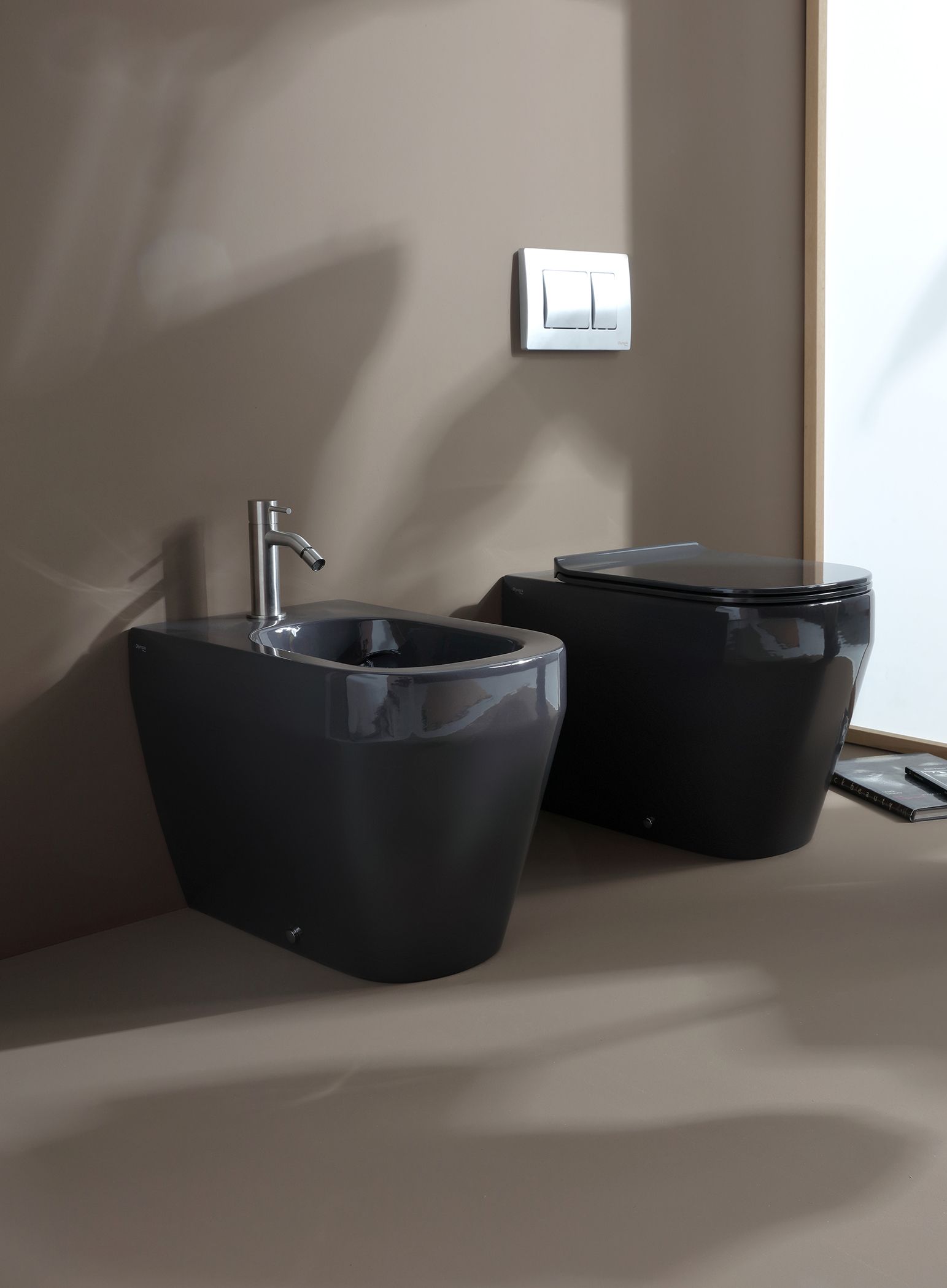WC e bidet neri sospesi in un bagno con parete neutra, pulsante di scarico e rubinetto.