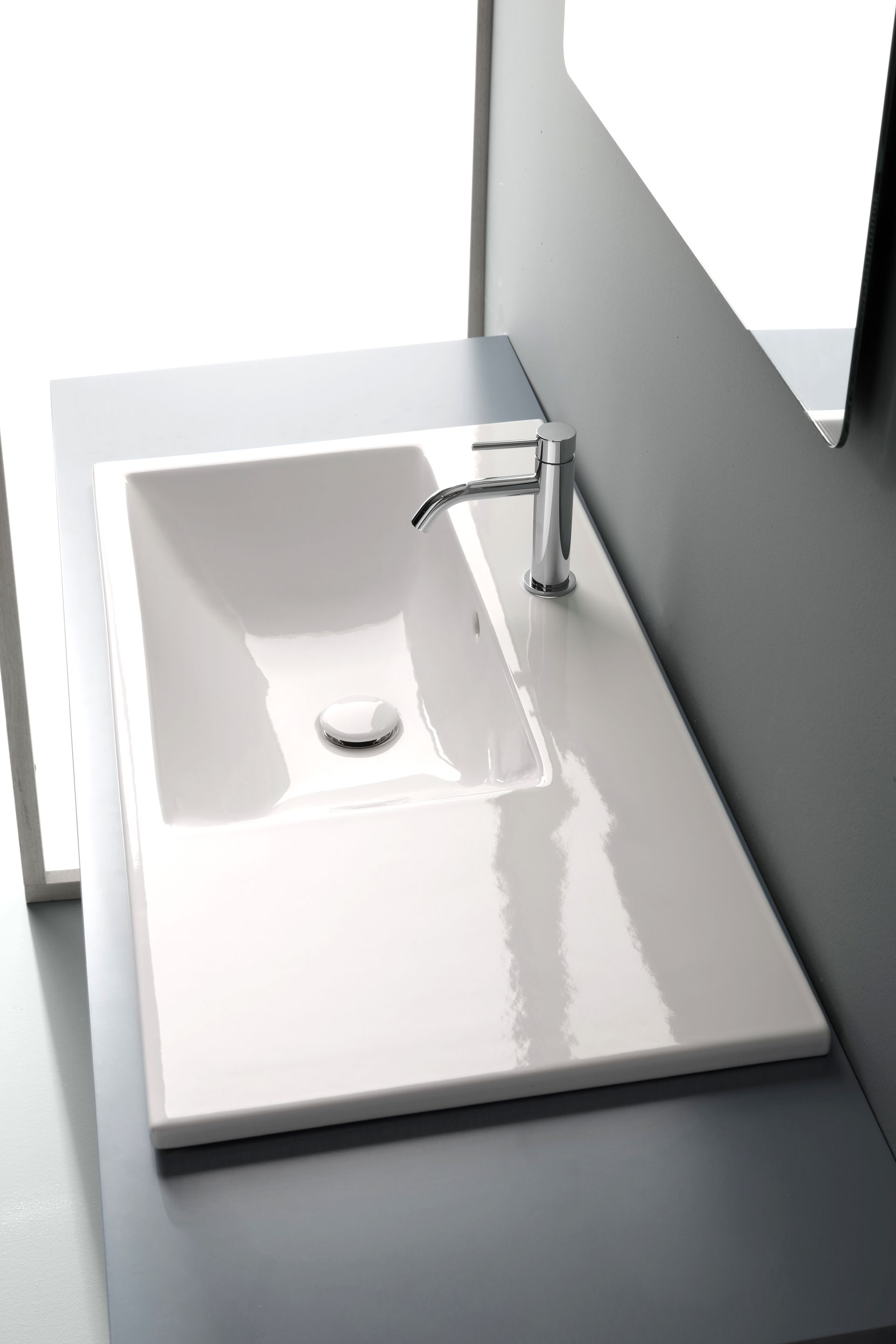 Lavandino rettangolare bianco con rubinetto cromato inserito in un piano di lavoro bianco.