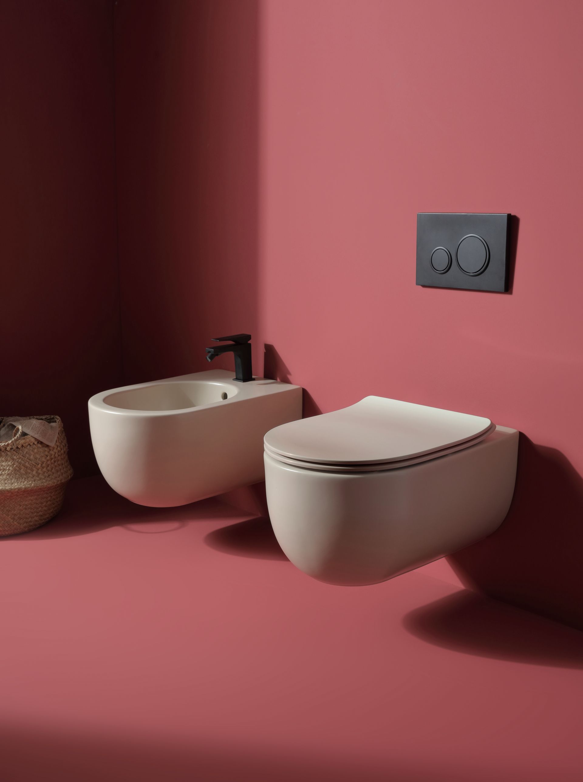 Moderno water e bidet beige su una parete rosa. Sono visibili una placca di scarico e un rubinetto neri.