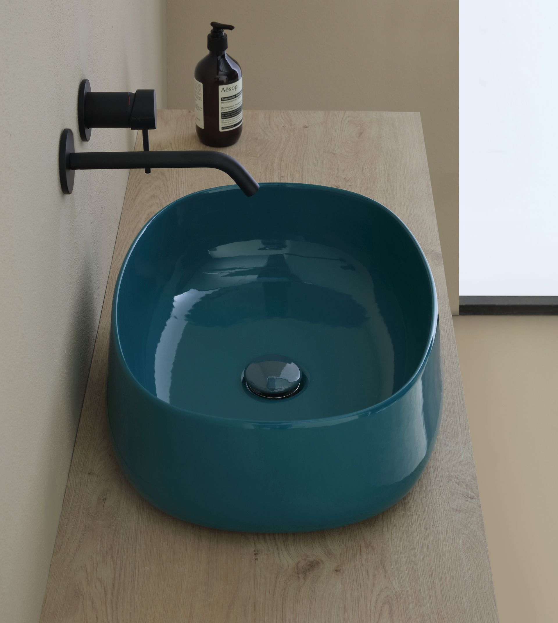Lavandino color verde acqua su ripiano in legno con rubinetto nero e dispenser per il sapone.