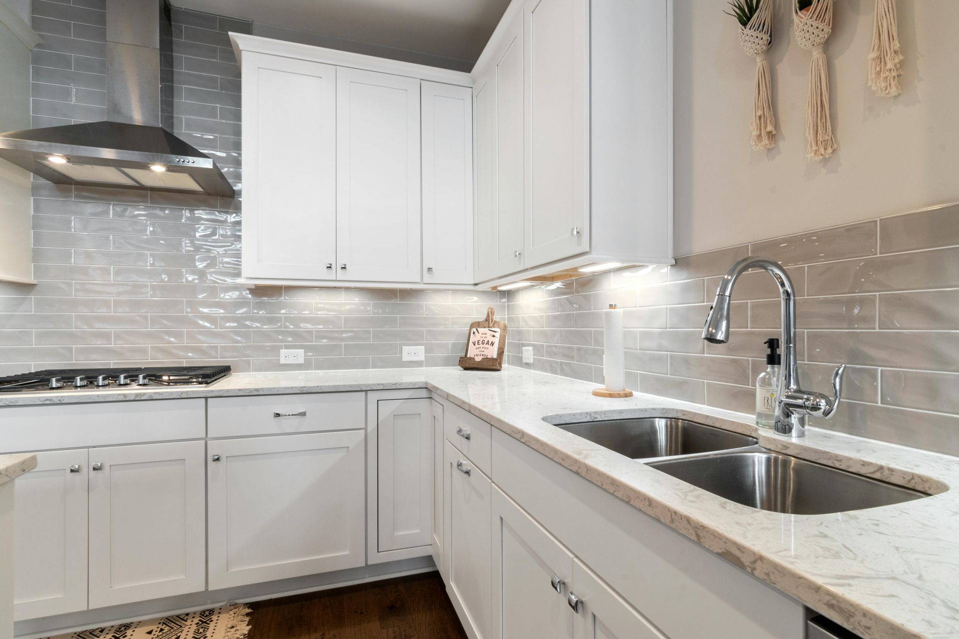 White kitchen with gray tile backsplash, stainless steel appliances, and double sink.