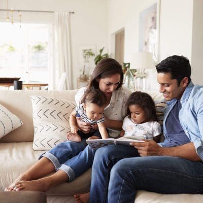 A family is sitting on a couch reading a book together.