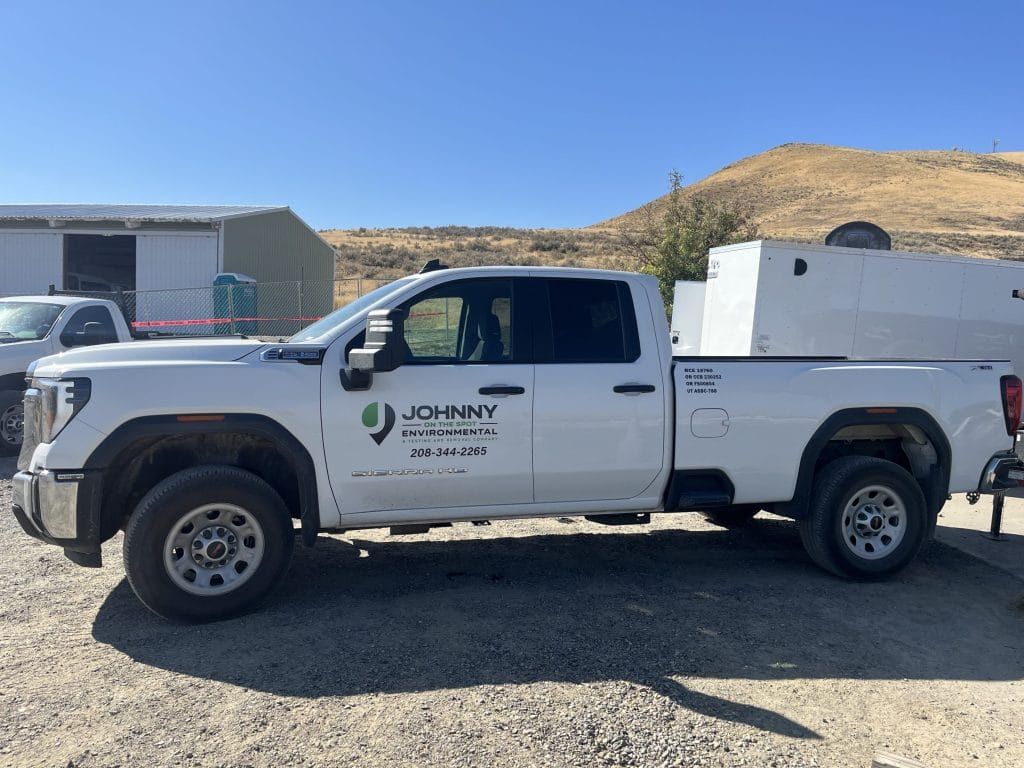 A white pickup truck is parked in a gravel lot with a Johnny on the Spot logo.