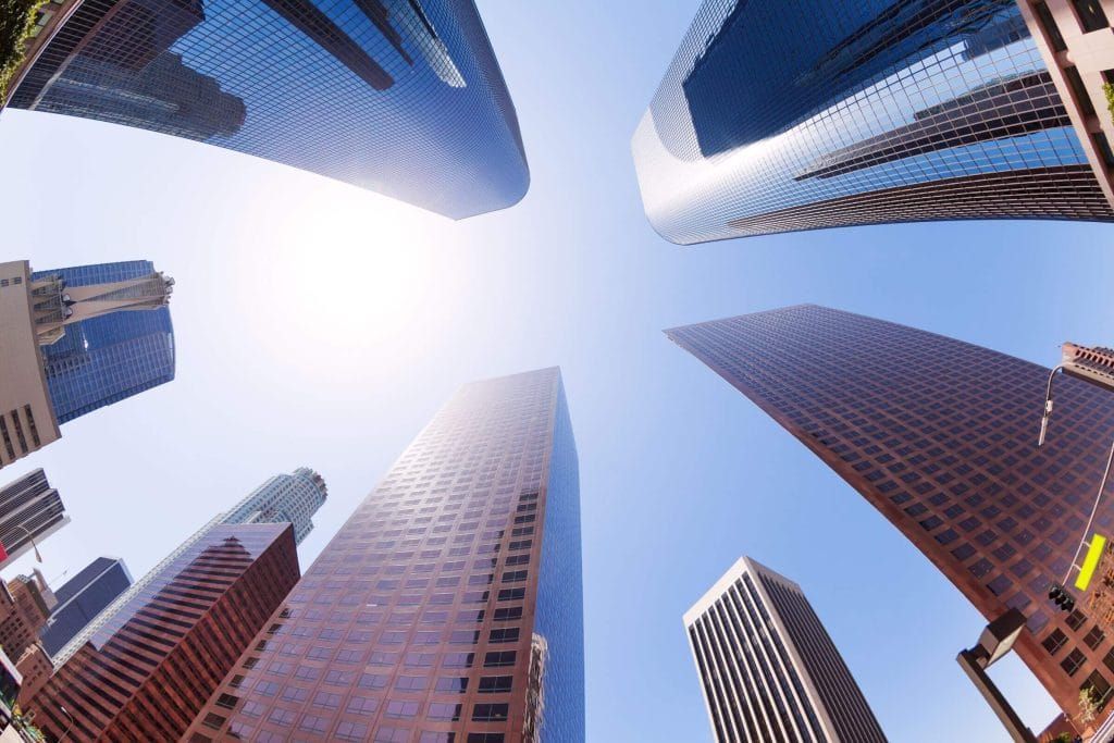 Looking up at a group of skyscrapers with the sun shining through them in a commercial area.
