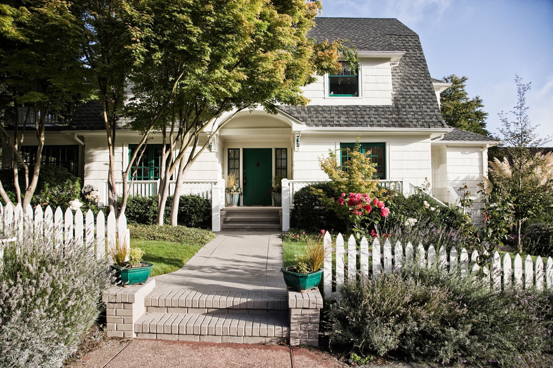 White house with a green door, picket fence, and garden.