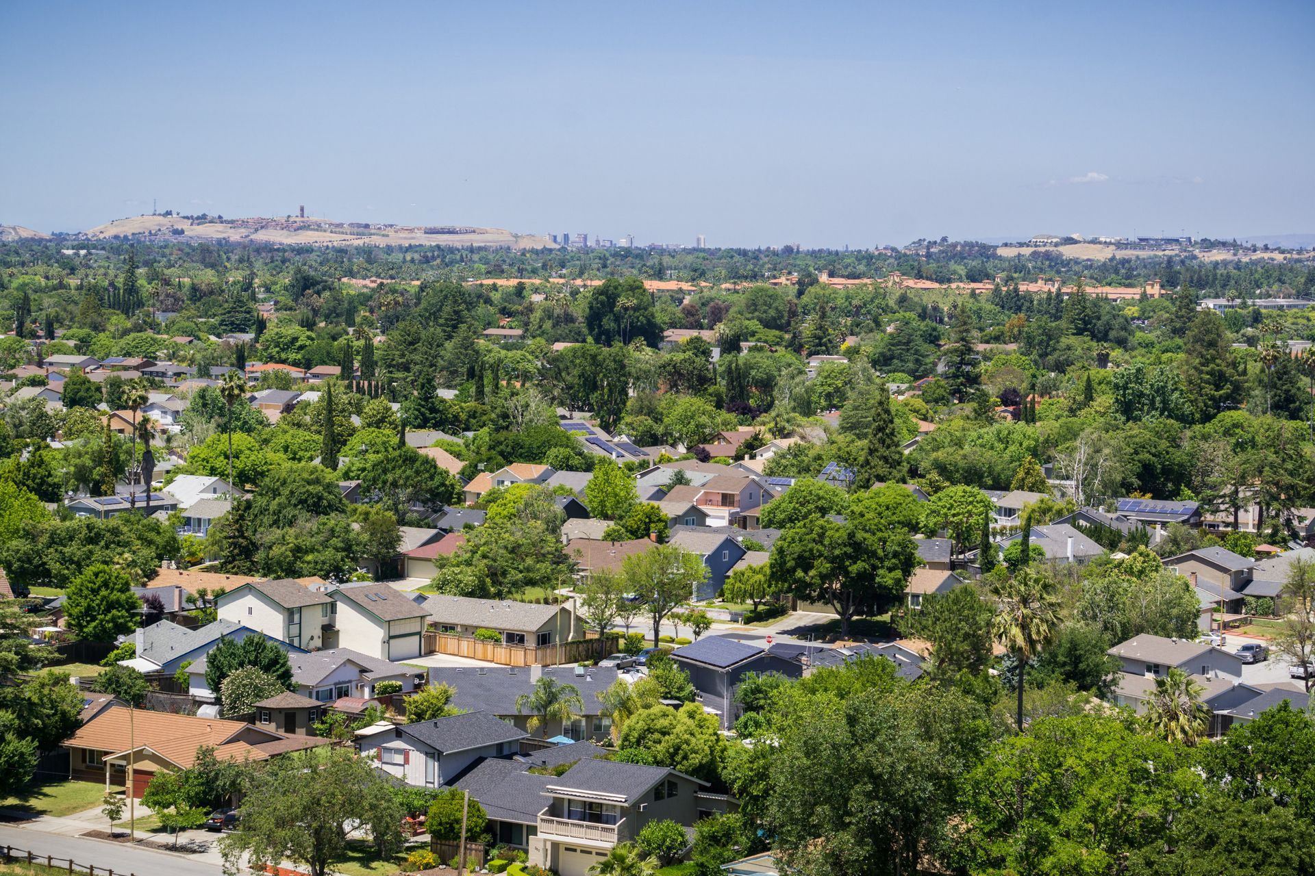Suburban neighborhood with houses nestled among lush green trees under a clear blue sky.