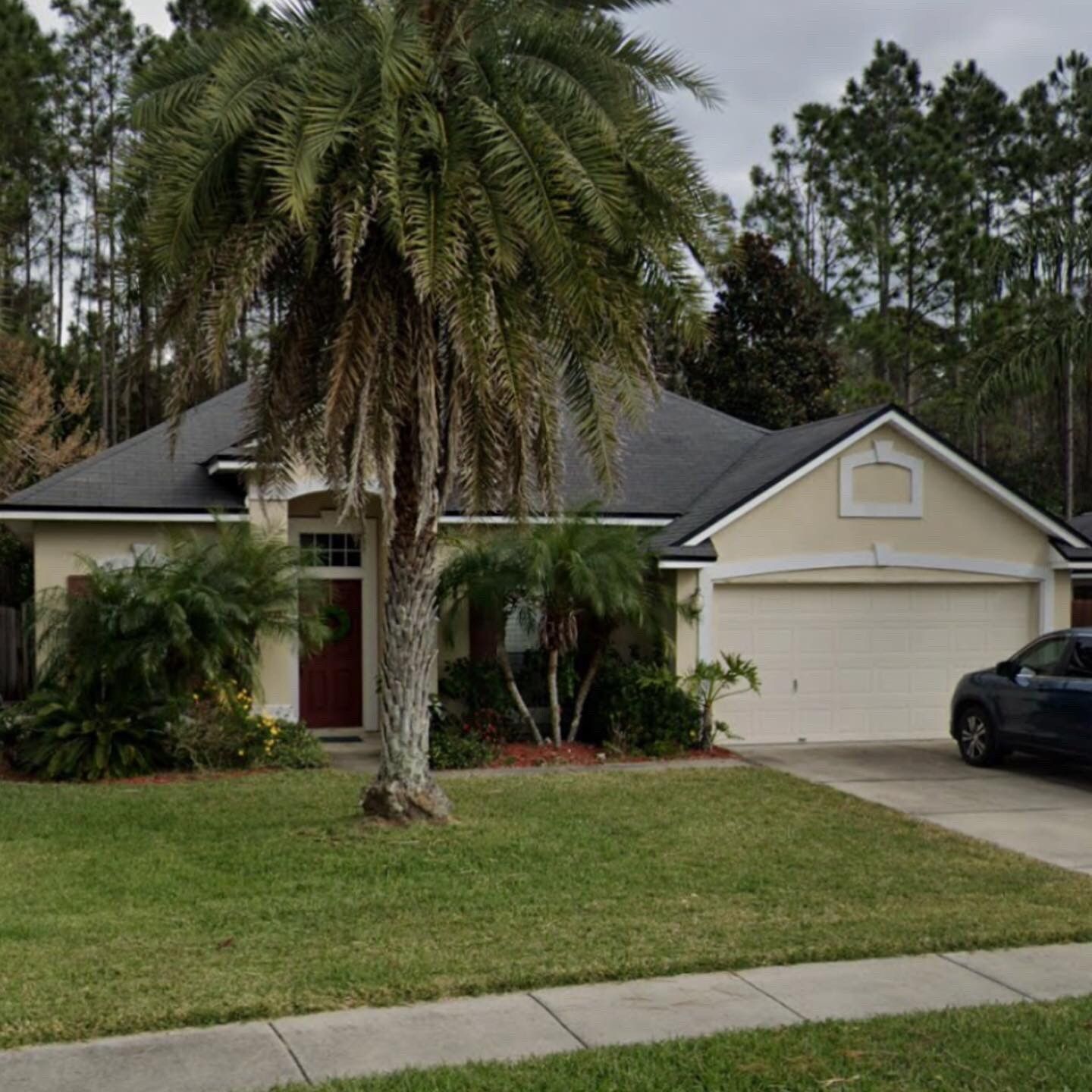 A car is parked in front of a house with a palm tree