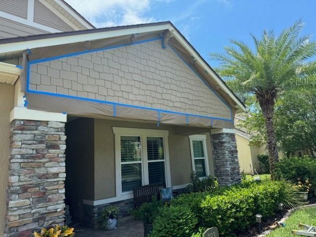 The front of a house is being painted with blue tape.