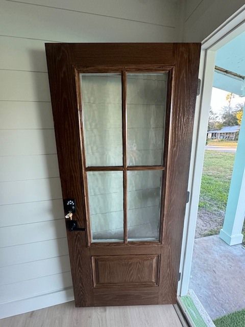 A wooden door with a glass window is open to a porch.